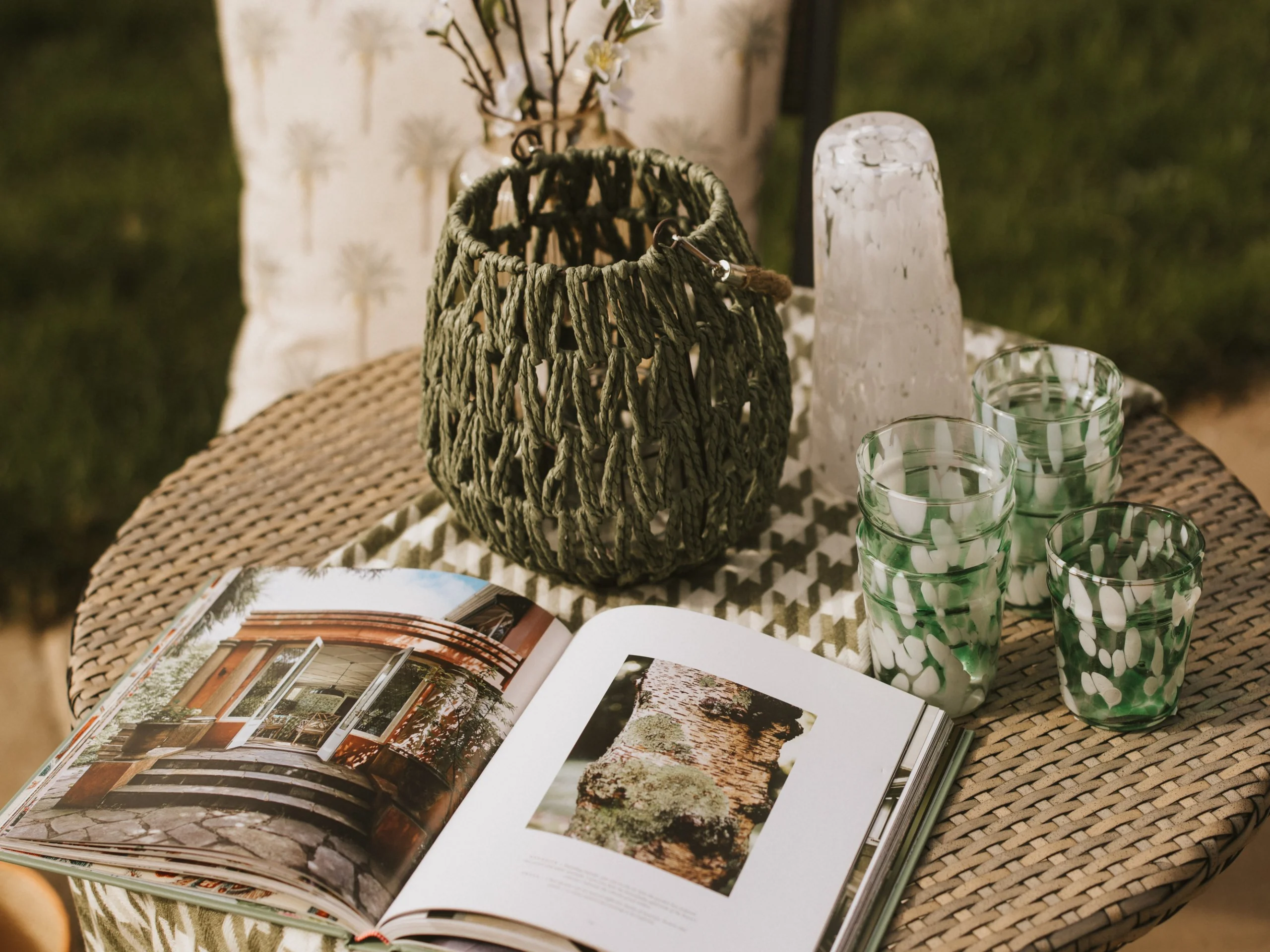 an interior design book on an outdoor table with green glasses and white flowers