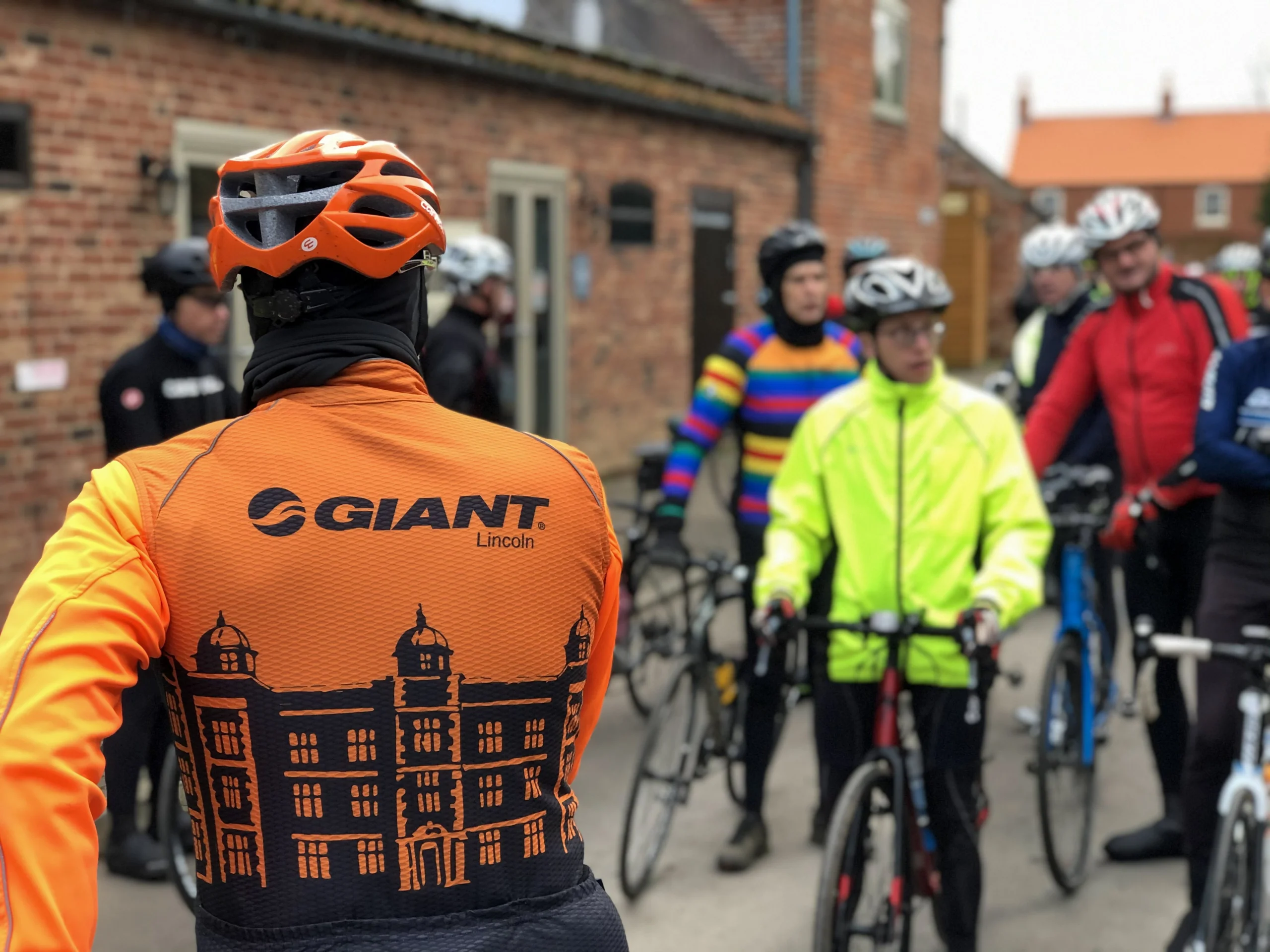 a group of cyclists with one wearing an orange giant lincoln jersey top in the foreground
