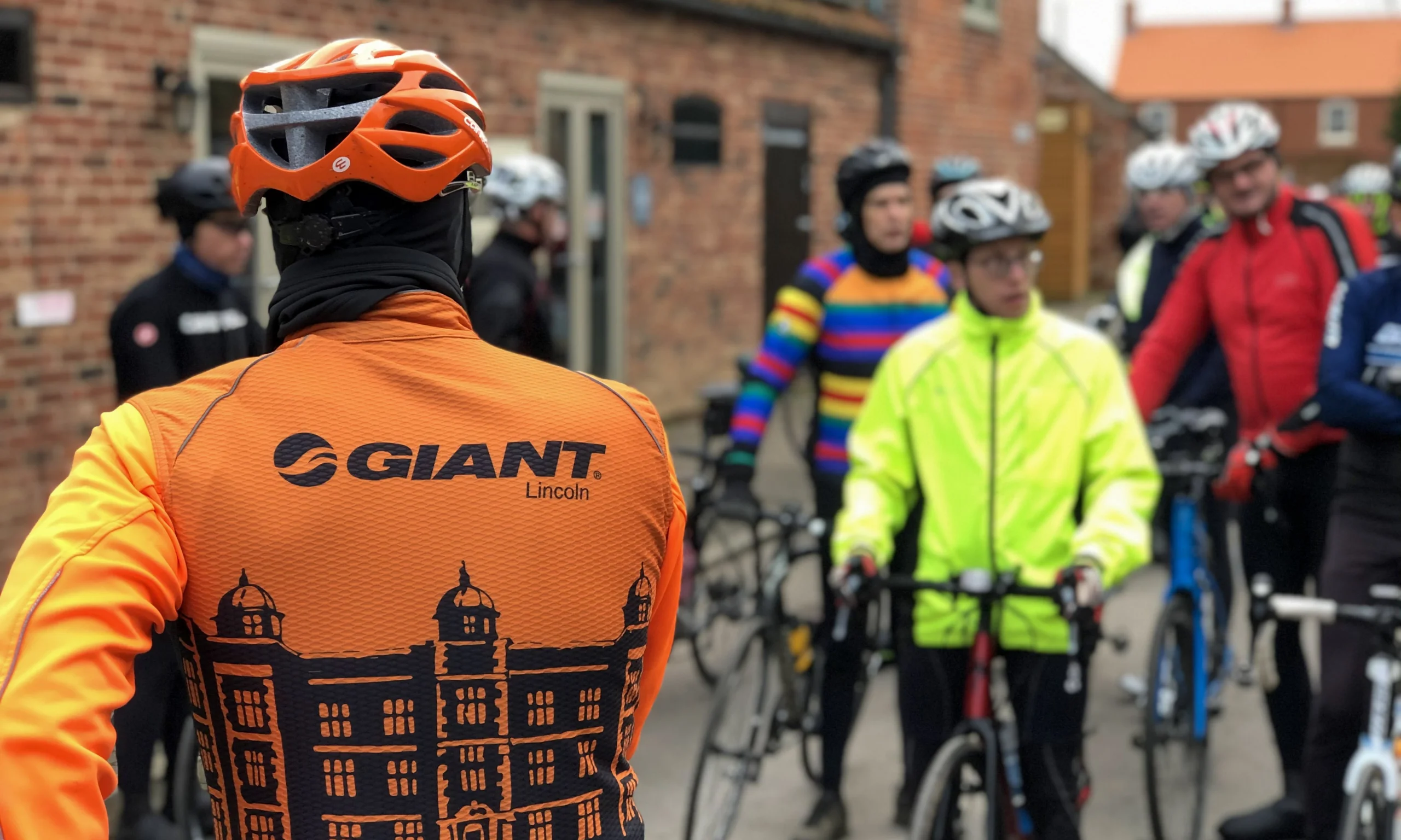 a group of cyclists with one wearing an orange giant lincoln jersey top in the foreground