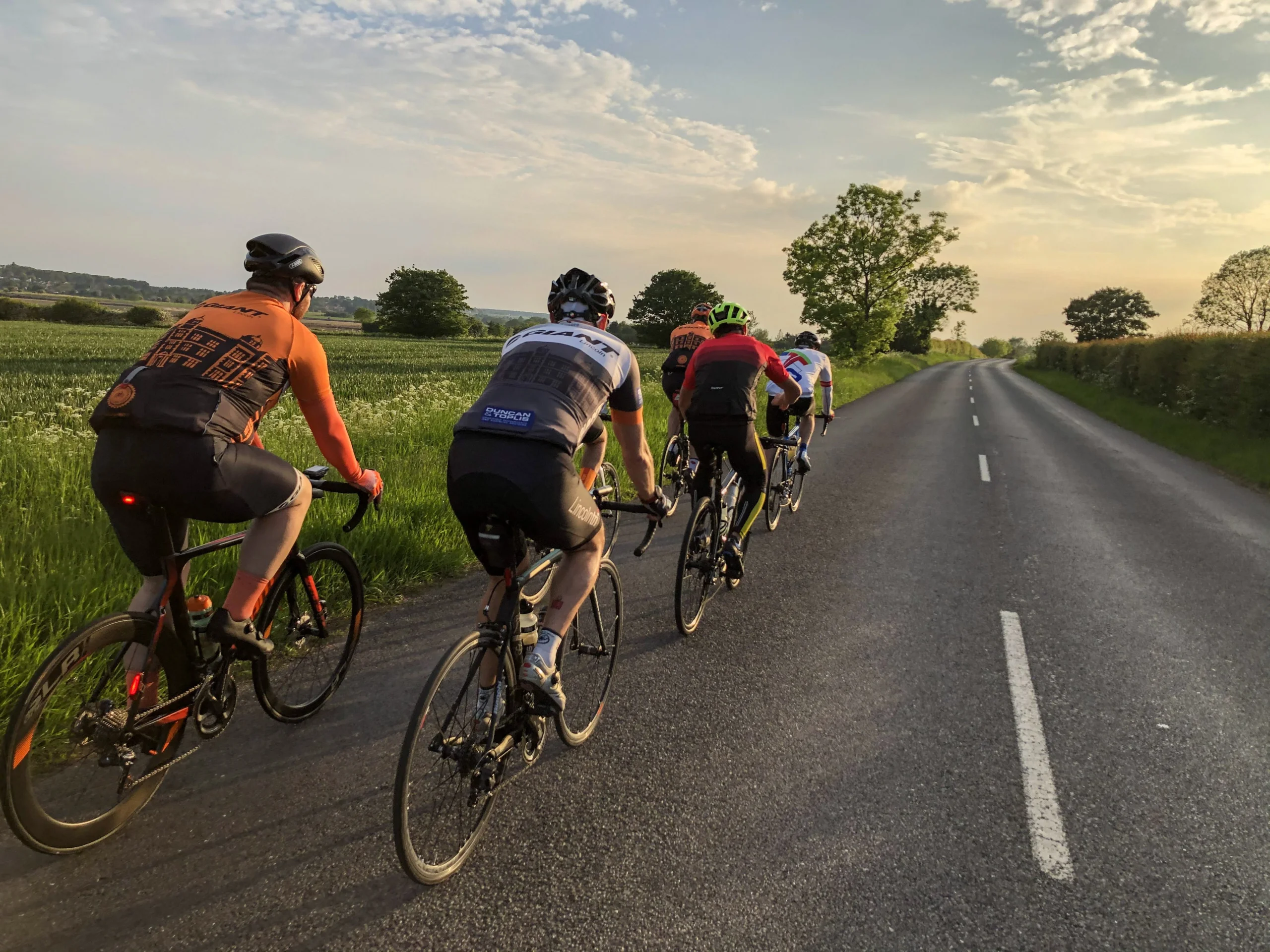 a small group of cyclists on the road in lincoln with a sunset background