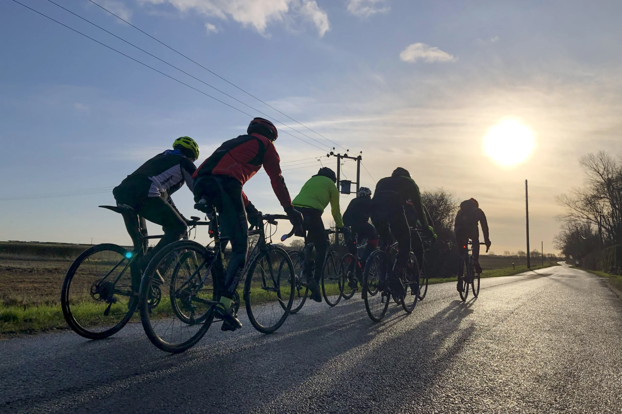 a group of cyclists on a lincolnshire road with the sun setting in the background