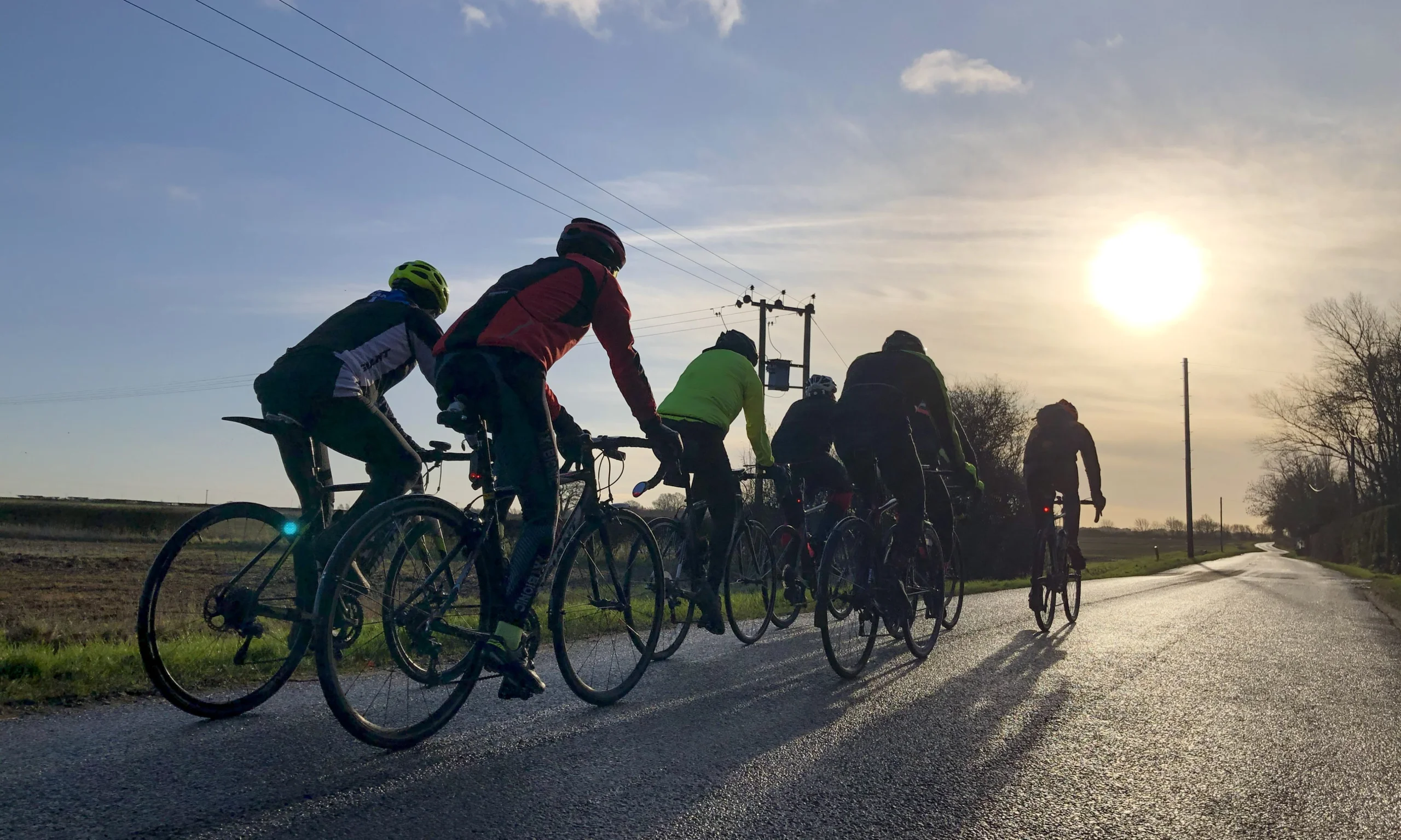 a group of cyclists on a lincolnshire road with the sun setting in the background