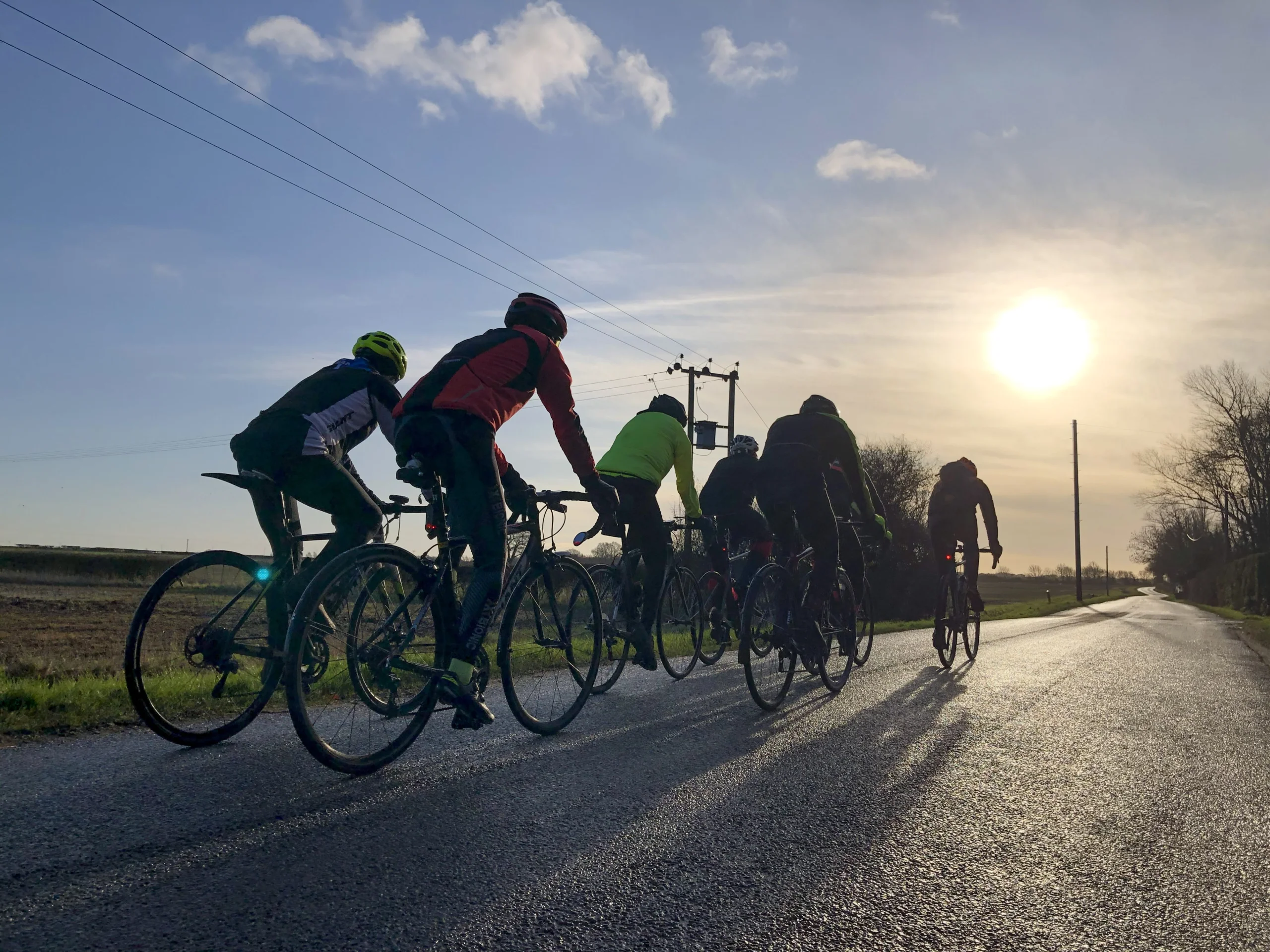 a group of cyclists on a lincolnshire road with the sun setting in the background