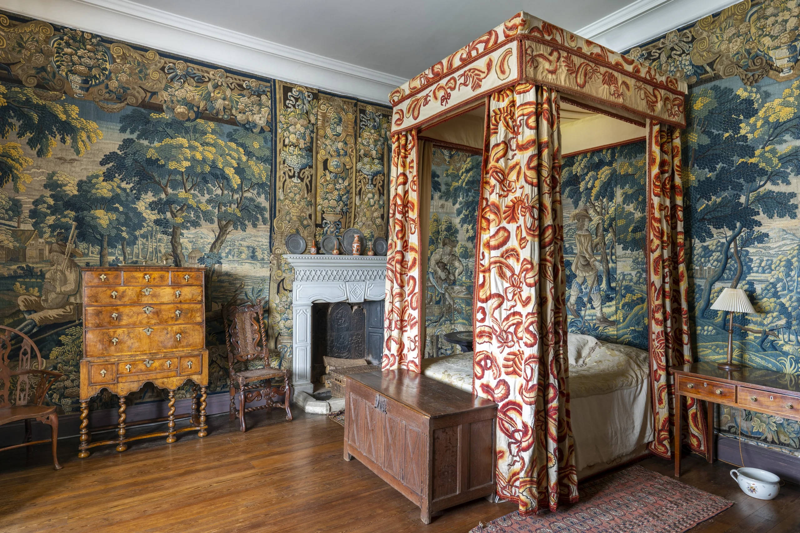A historic bedroom with tapestries hanging on the walls and an ornate four poster bed with curtains