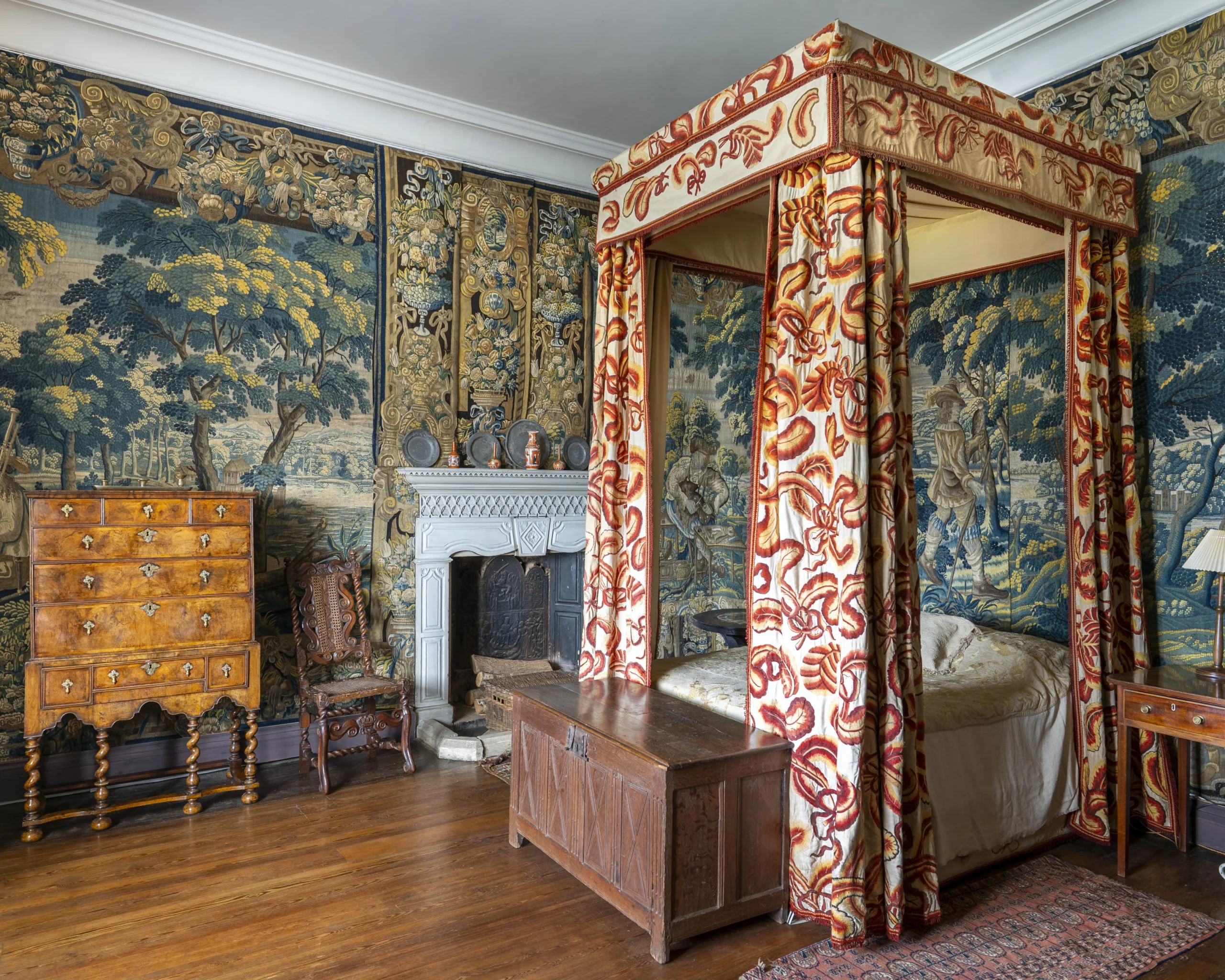 A historic bedroom with tapestries hanging on the walls and an ornate four poster bed with curtains