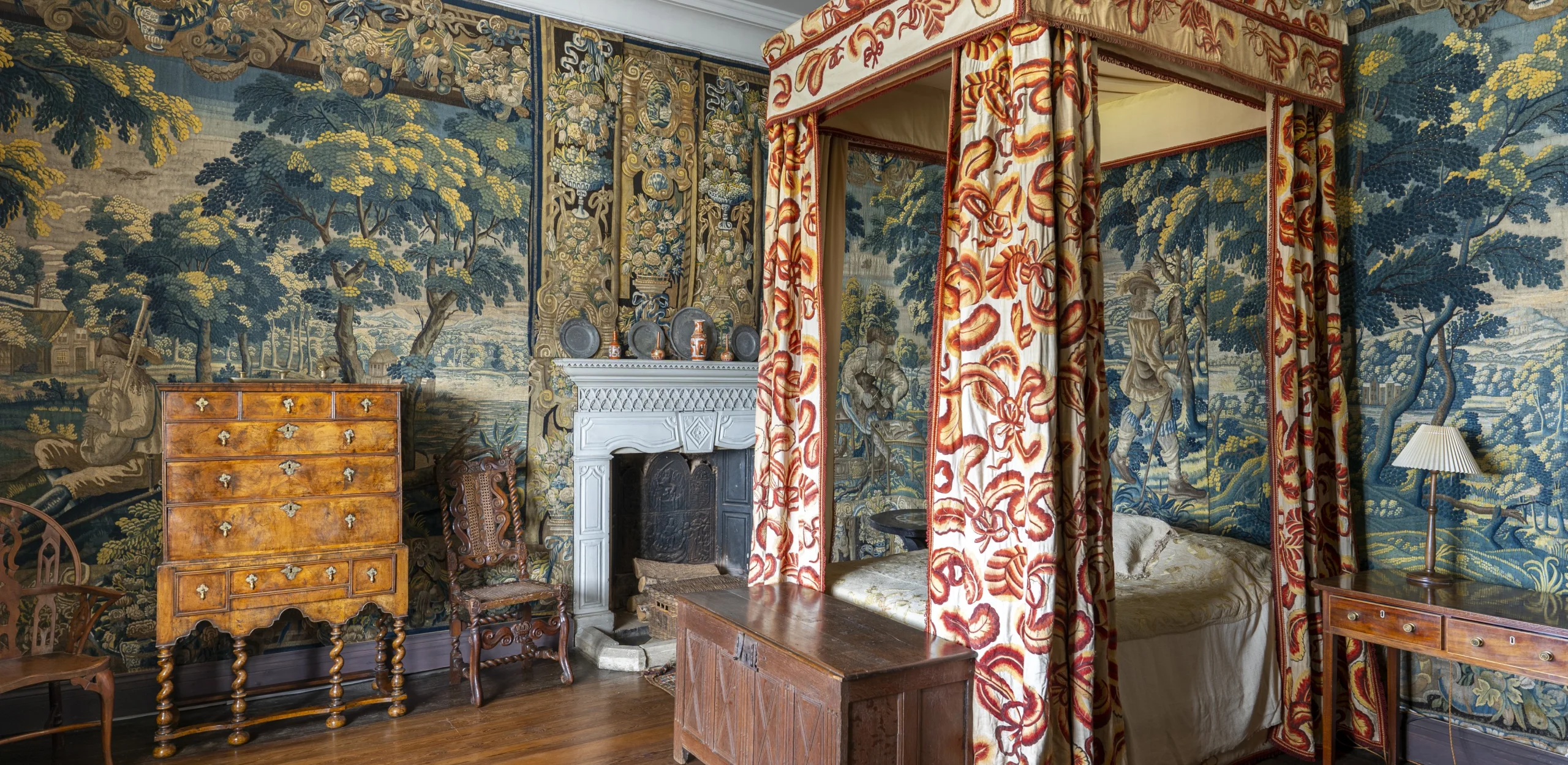 A historic bedroom with tapestries hanging on the walls and an ornate four poster bed with curtains