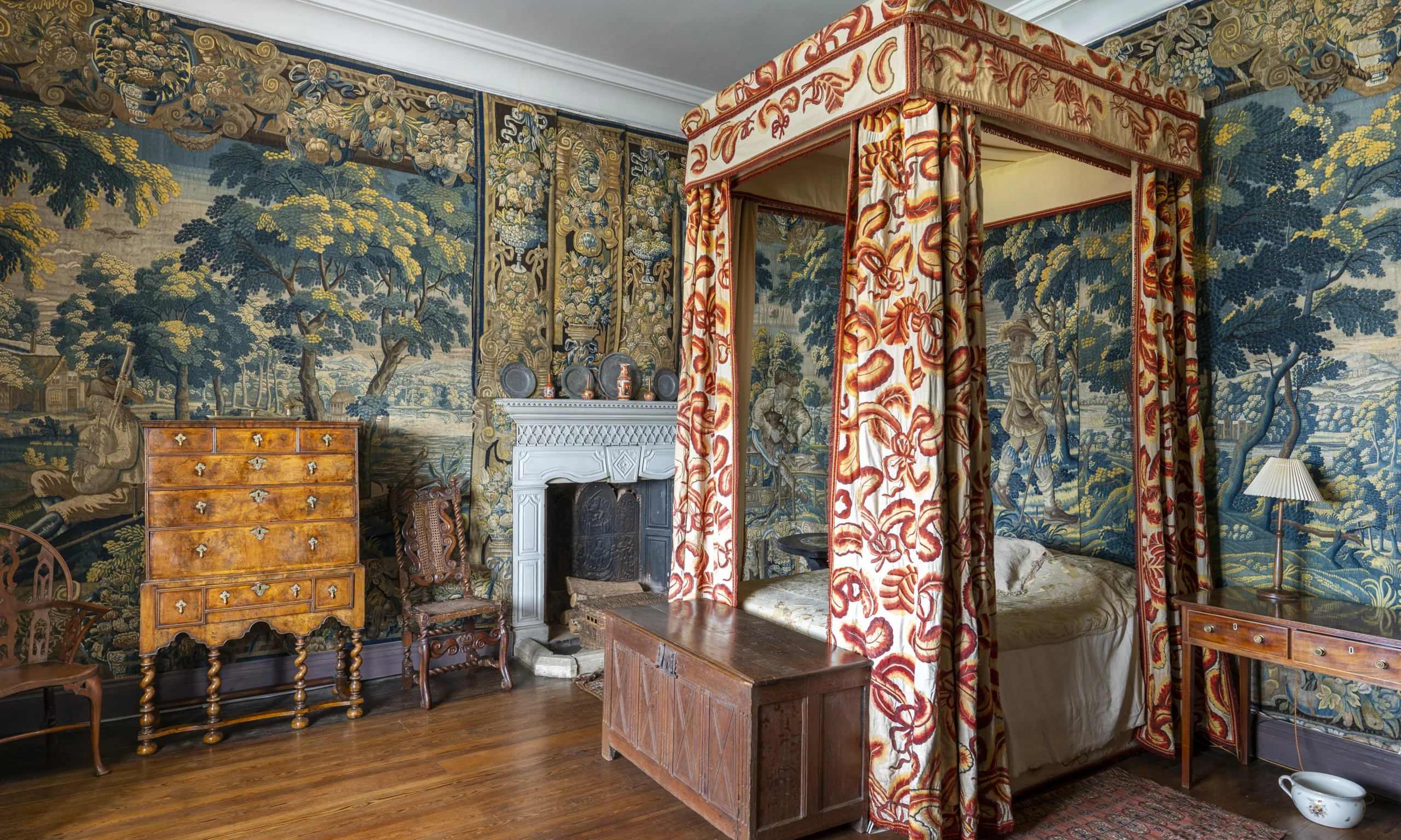 A historic bedroom with tapestries hanging on the walls and an ornate four poster bed with curtains