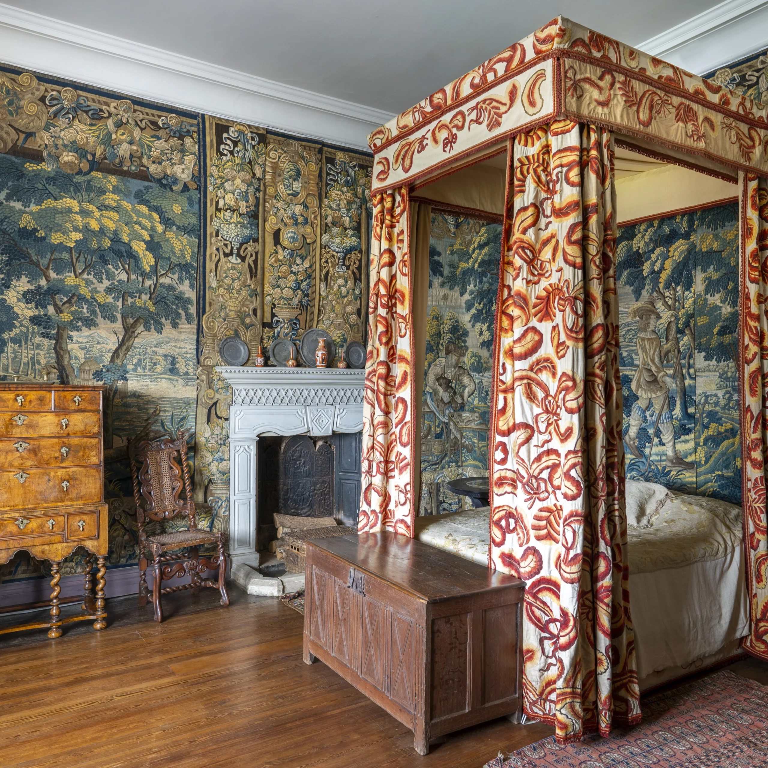 A historic bedroom with tapestries hanging on the walls and an ornate four poster bed with curtains