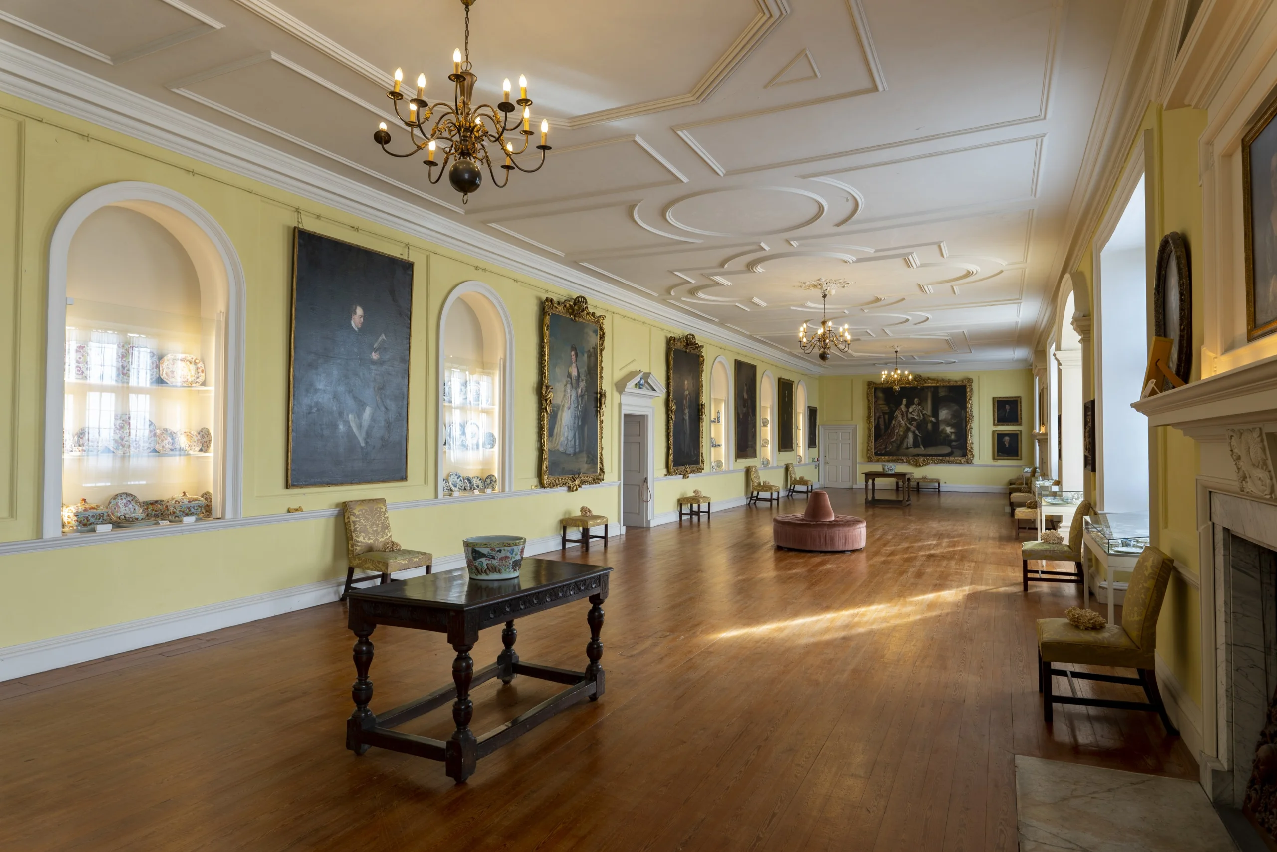 A long yellow gallery room adorned with antique portraits and furniture