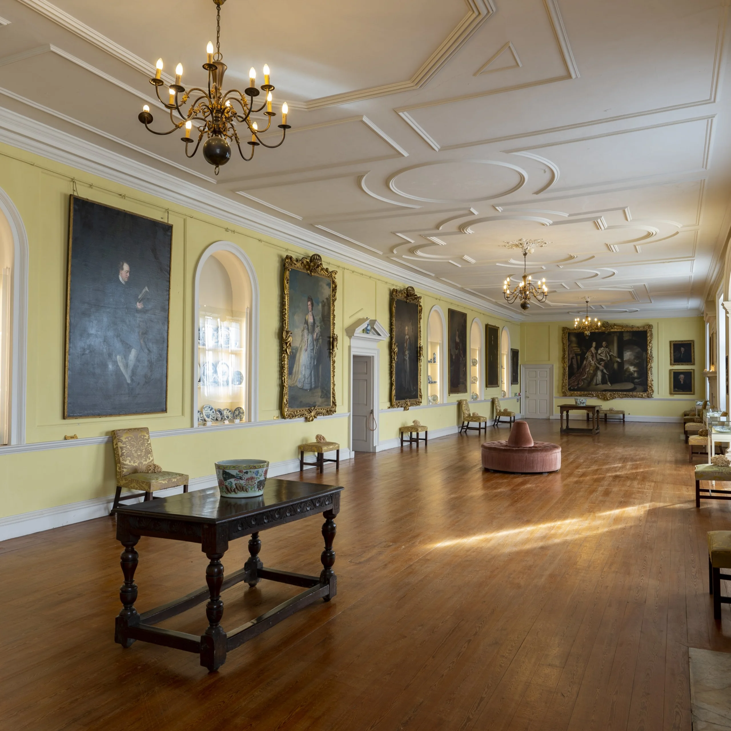 A long yellow gallery room adorned with antique portraits and furniture