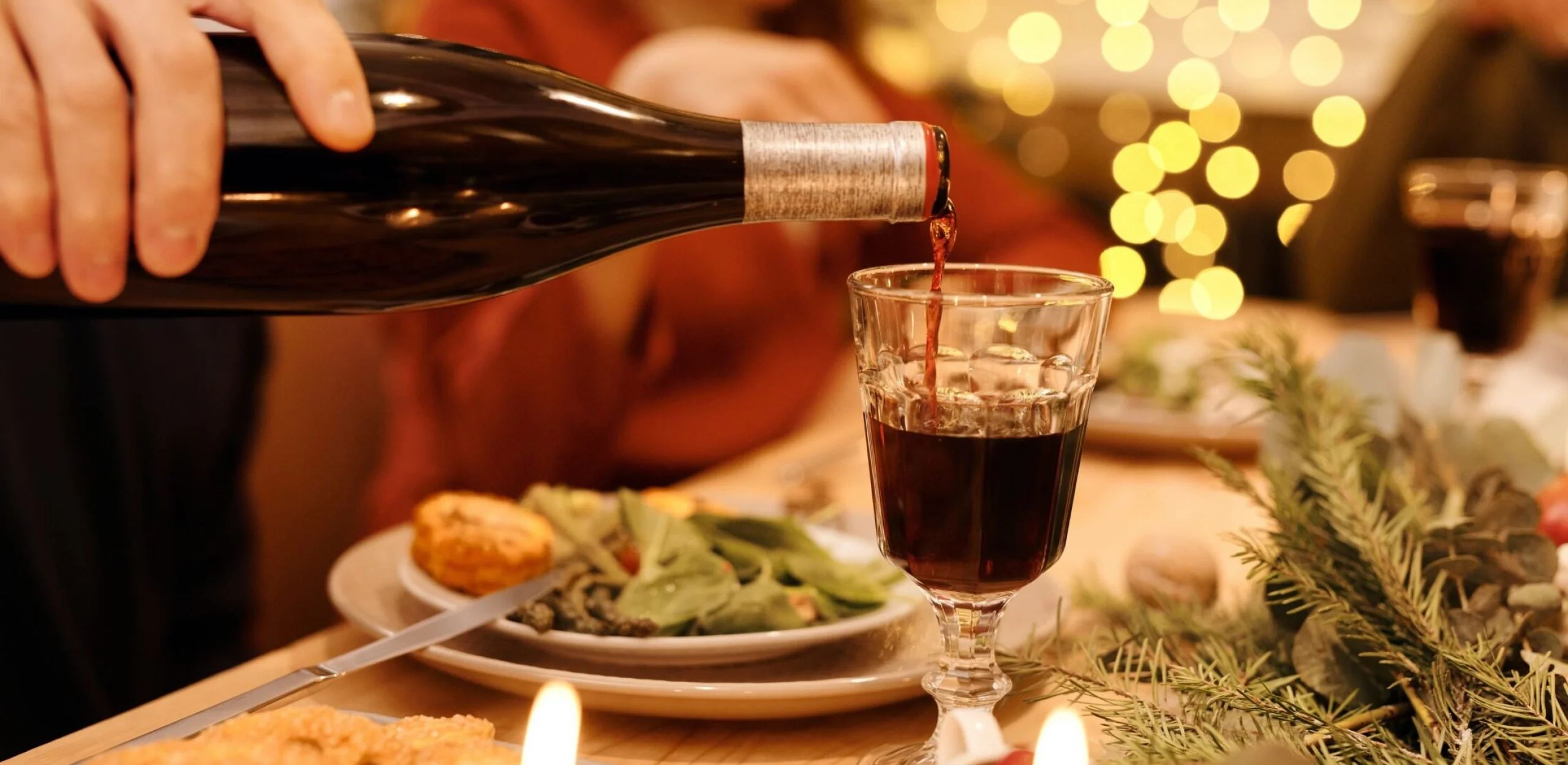 someone pouring red wine from a bottle into a glass with christmas lights in the background