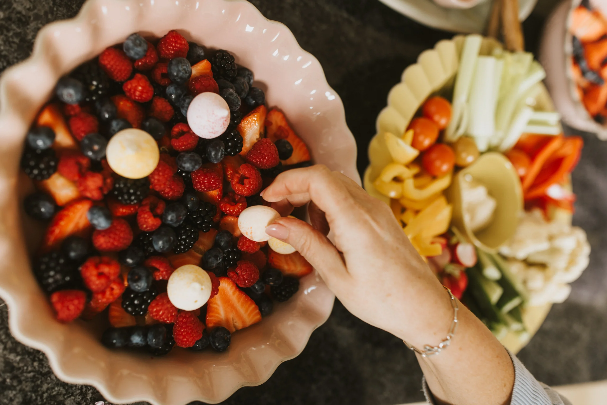 A hand reaches into shot, selecting a summer berry from a bowl