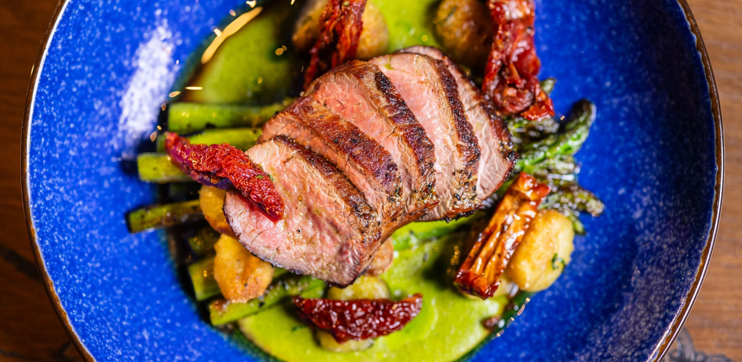 roasted lamb loin sliced on top of vegetables on a blue plate