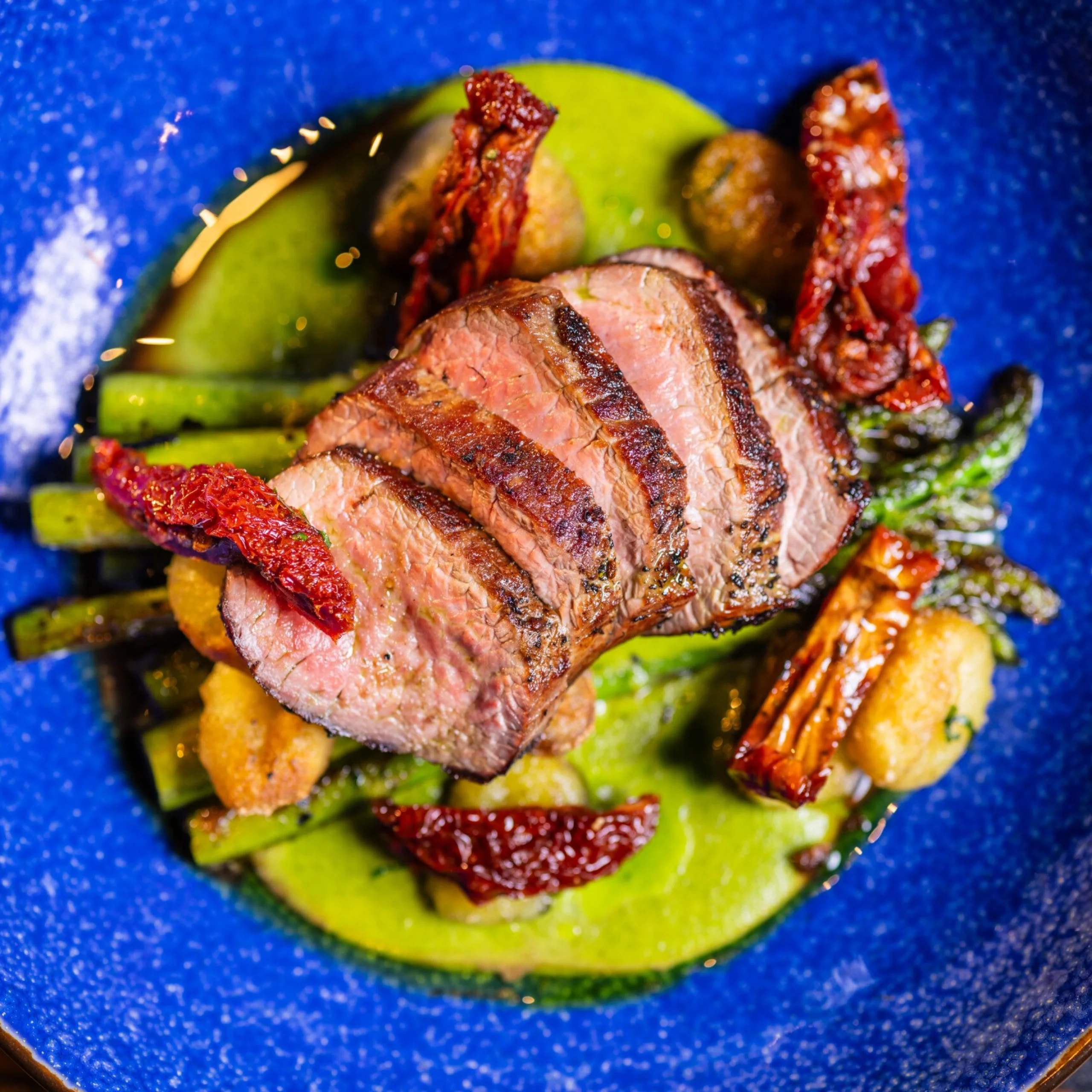 roasted lamb loin sliced on top of vegetables on a blue plate