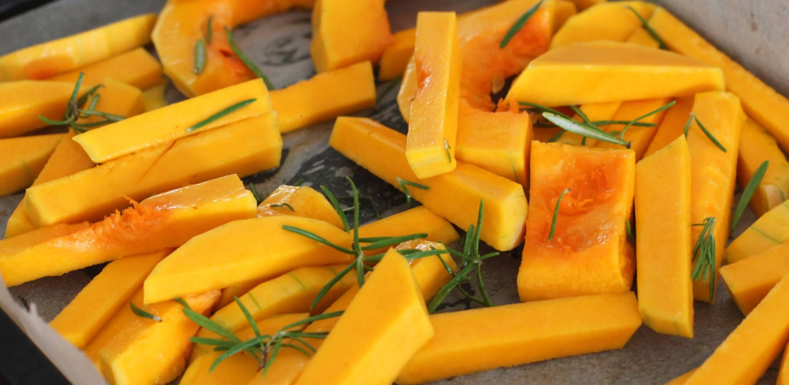 slices of butternut squash on a roasting tray with rosemary