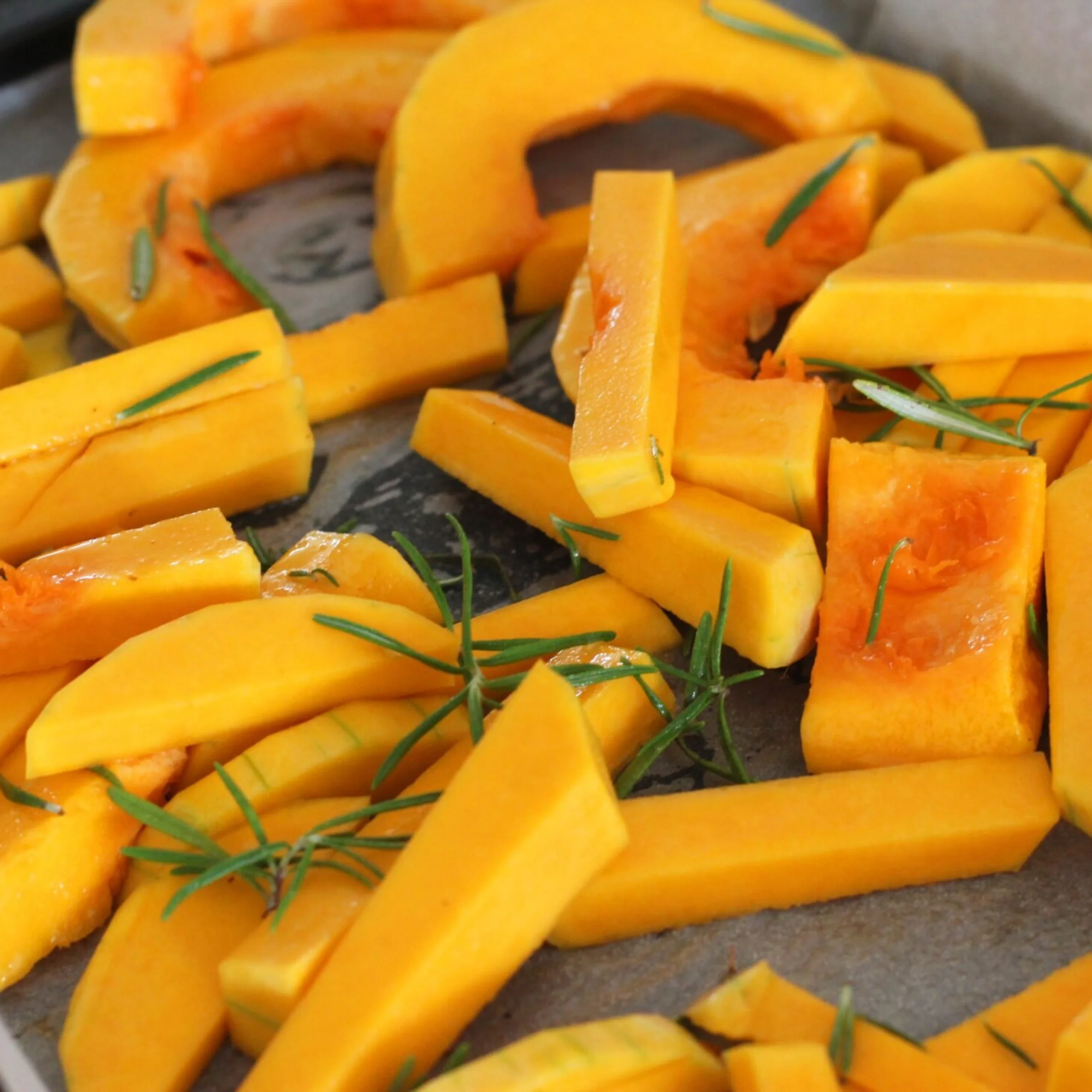 slices of butternut squash on a roasting tray with rosemary