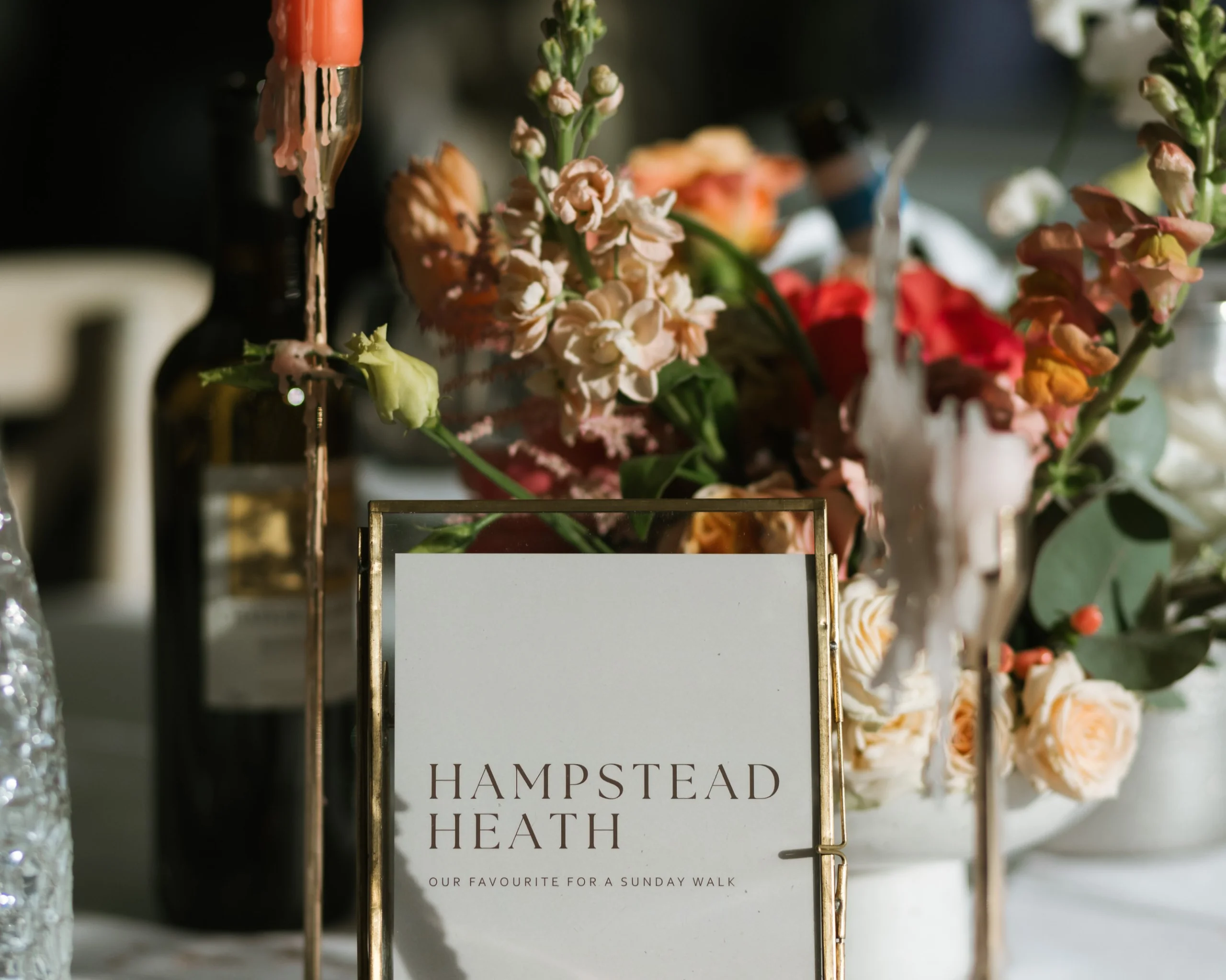 a wedding table setup with a table name and seasonal orange and peach flowers with an orange dinner candle in a gold holder