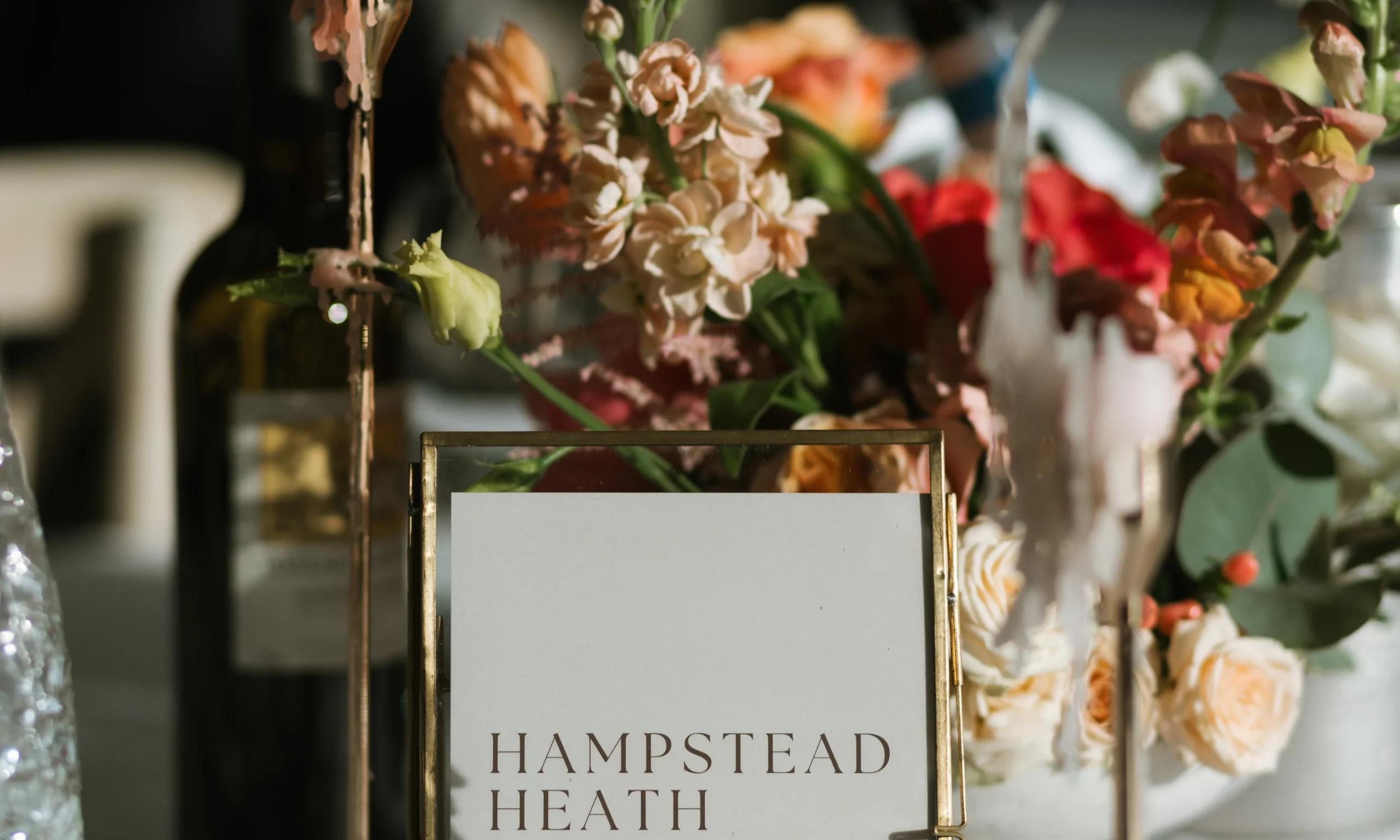 a wedding table setup with a table name and seasonal orange and peach flowers with an orange dinner candle in a gold holder
