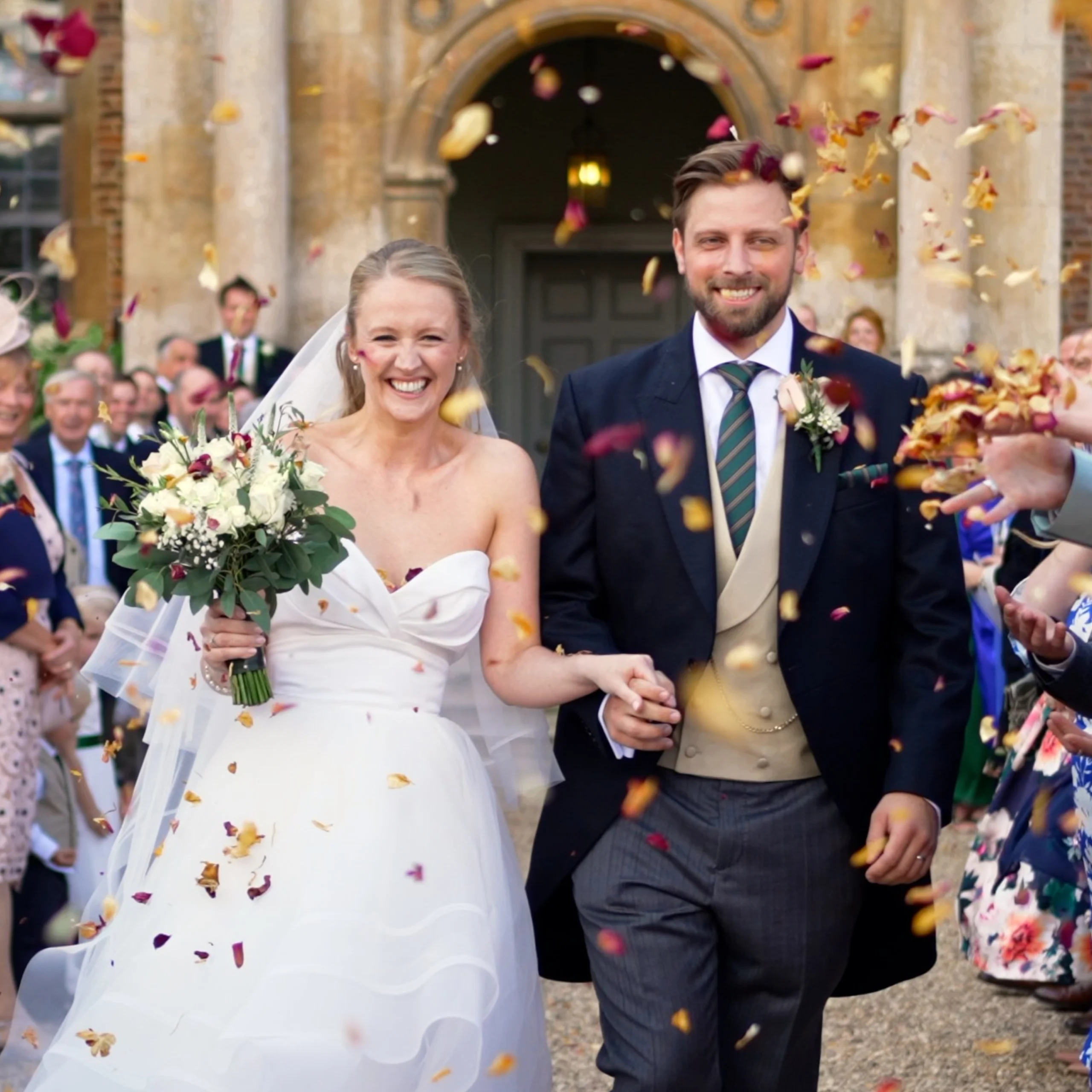 bride and groom holding hands under confetti outside historic house
