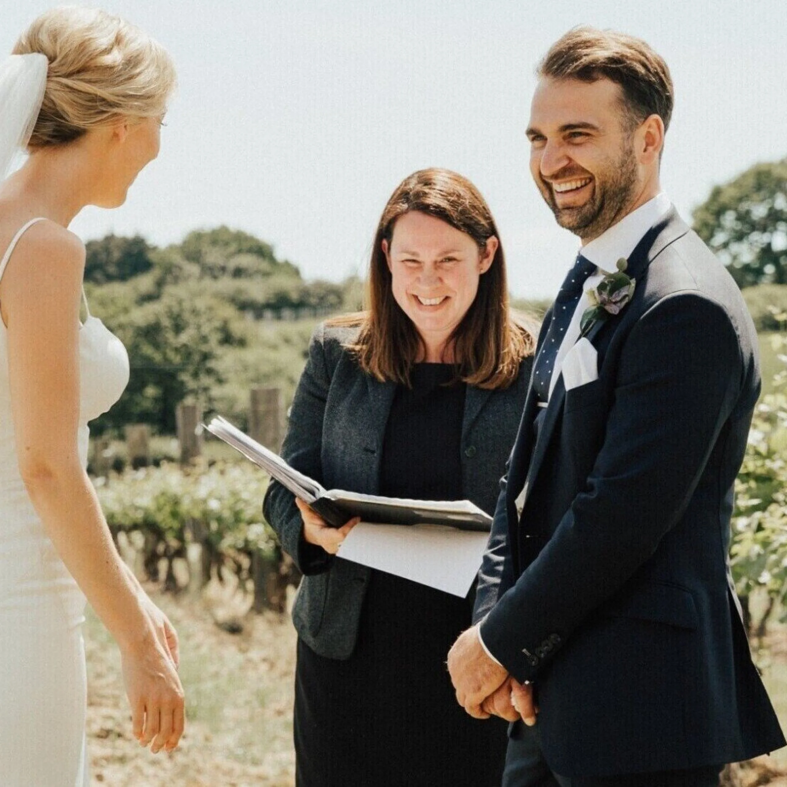 a bride groom and celebrant smiling at an outdoor wedding
