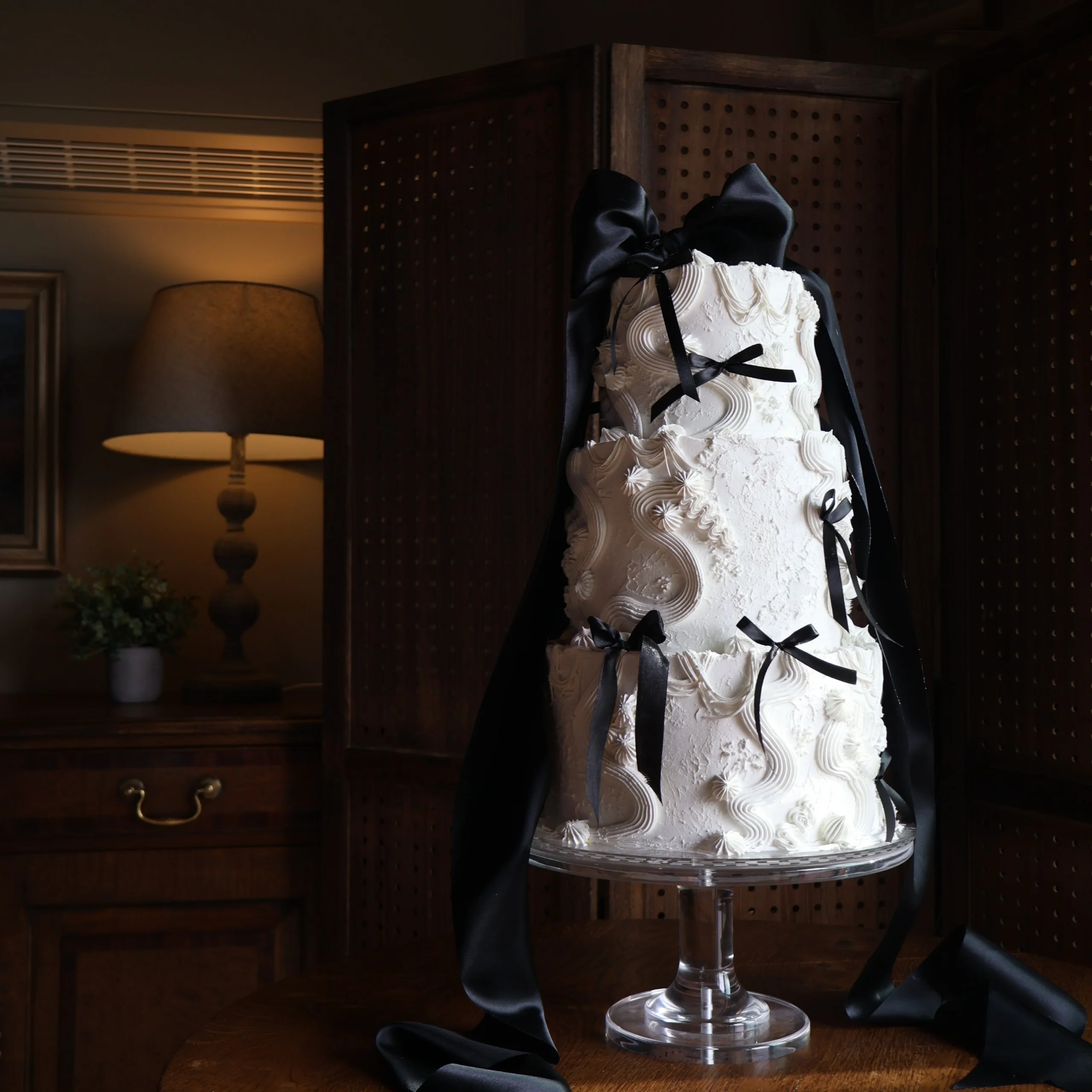 a white three tier wedding cake decorated with white icing piping and bows tied with black ribbon