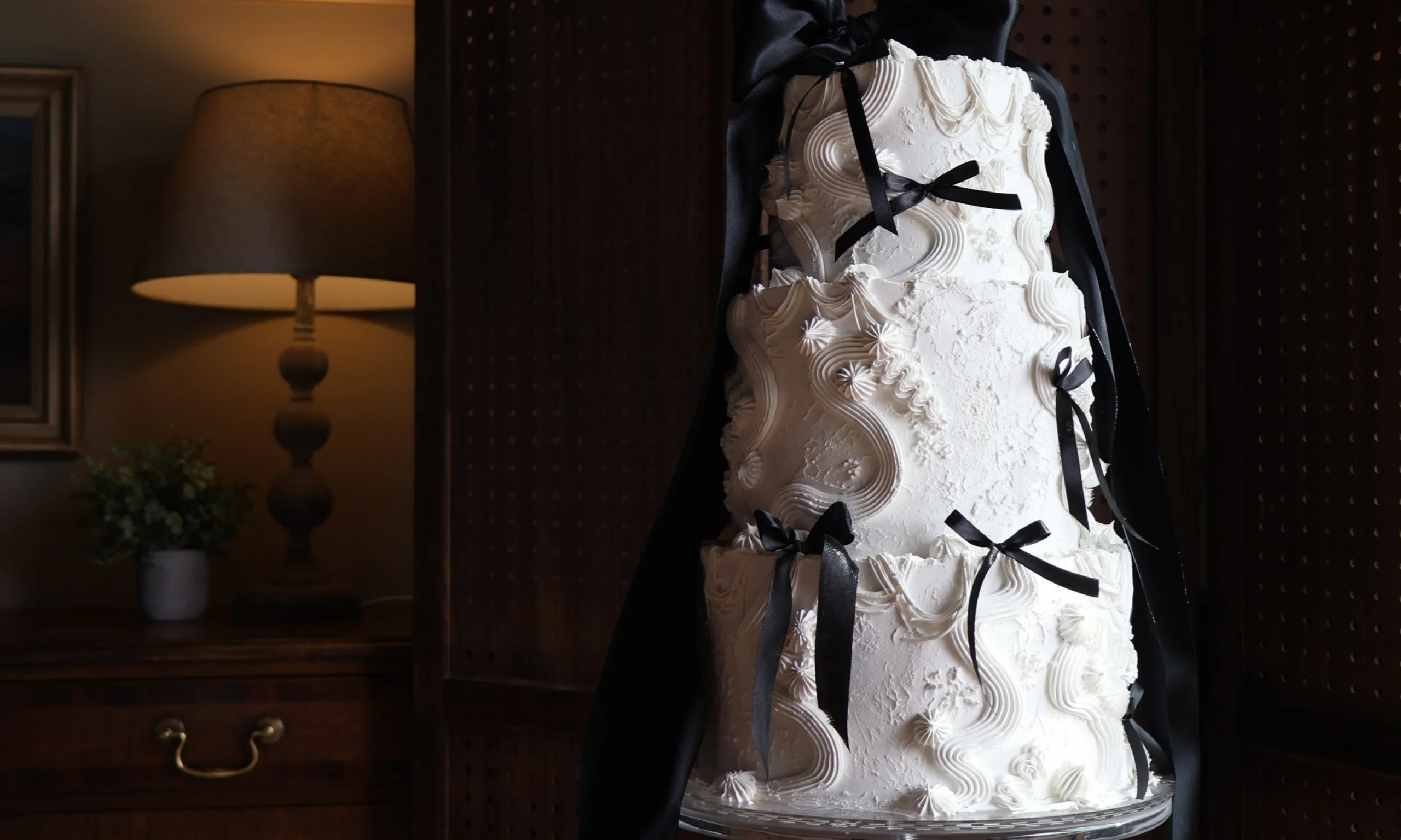 a white three tier wedding cake decorated with white icing piping and bows tied with black ribbon