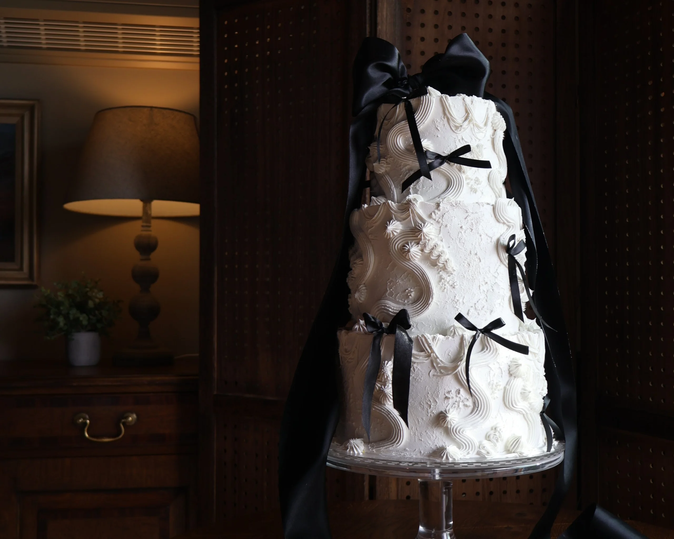 a white three tier wedding cake decorated with white icing piping and bows tied with black ribbon