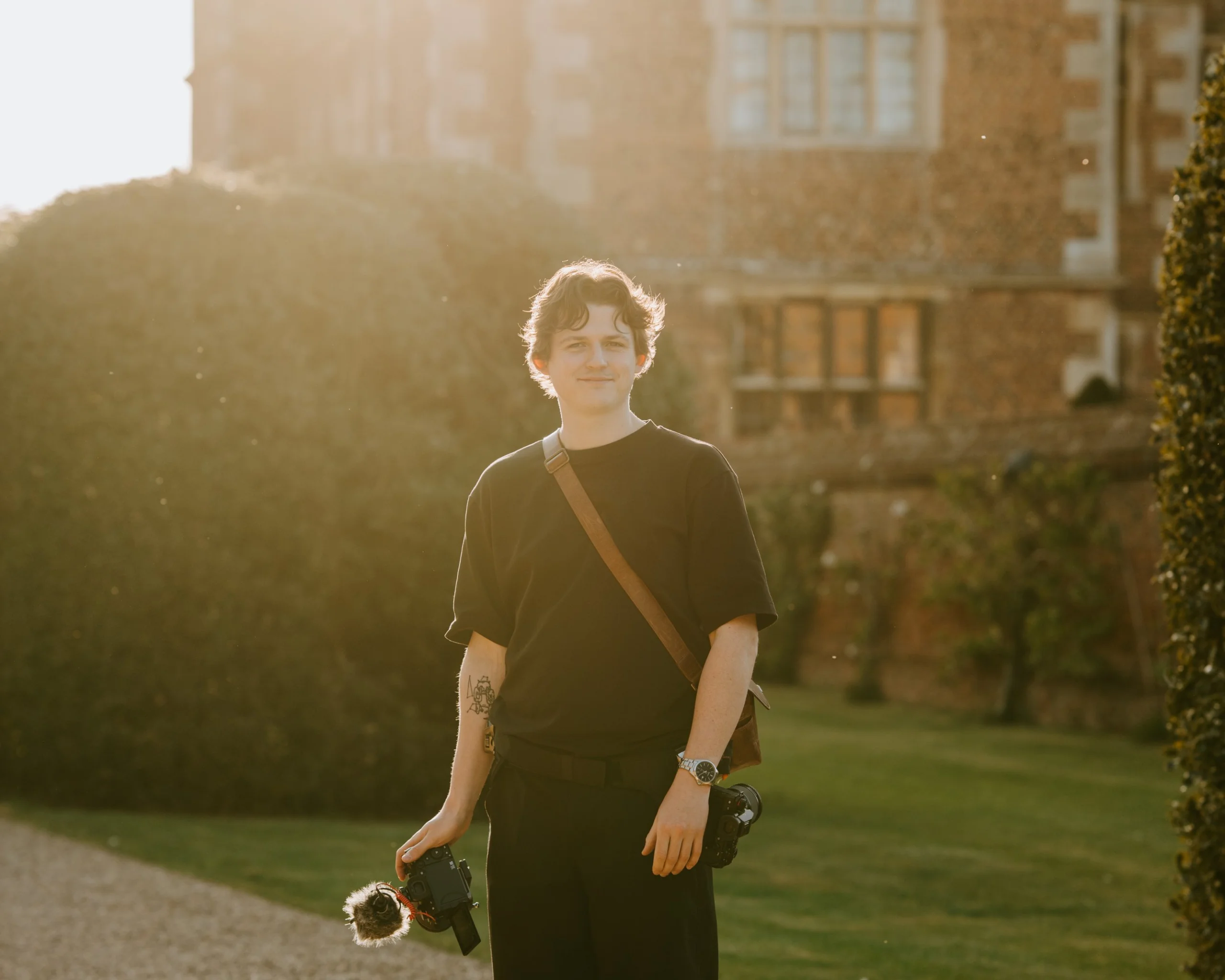 portrait photo of george hughes wedding photographer wearing black carrying cameras