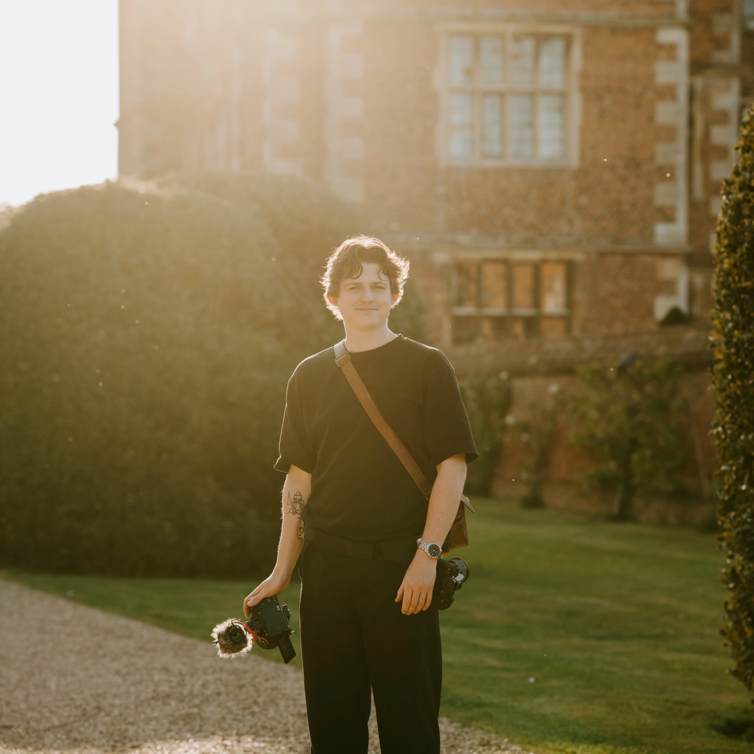 portrait photo of george hughes wedding photographer wearing black carrying cameras