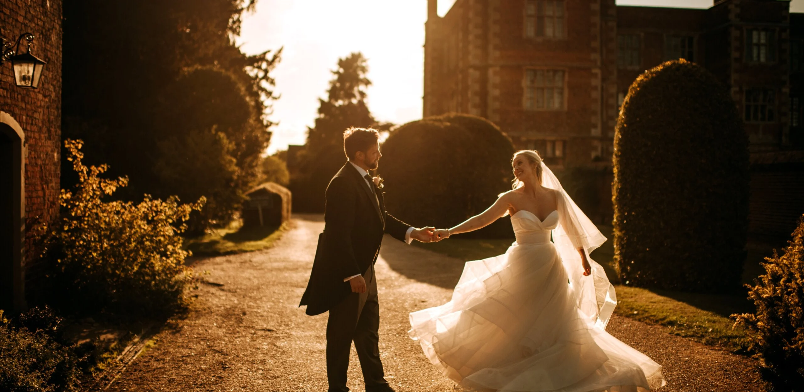 a bride and groom holding hands in the sunset with elizabethan hall in the background