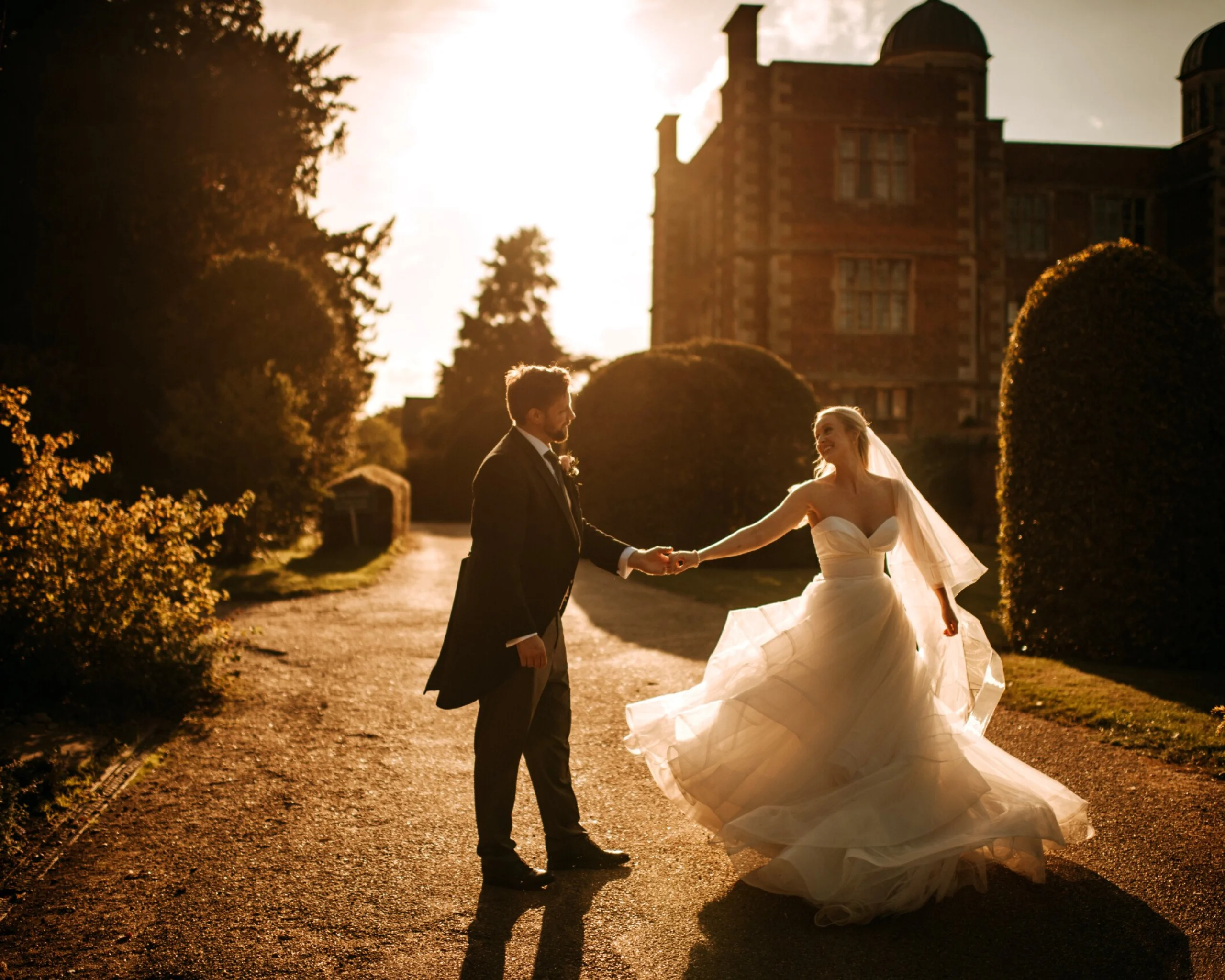 a bride and groom holding hands in the sunset with elizabethan hall in the background