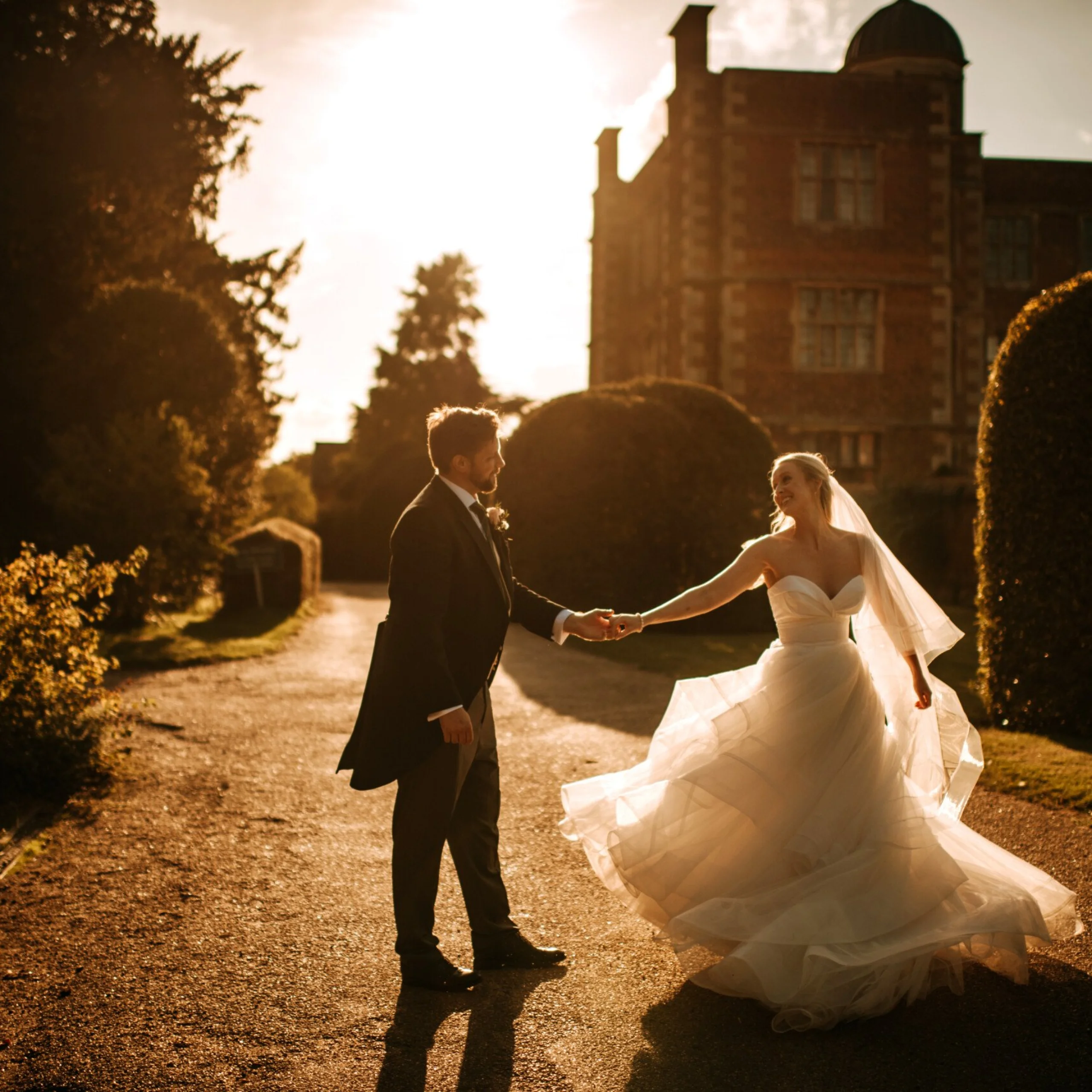 a bride and groom holding hands in the sunset with elizabethan hall in the background