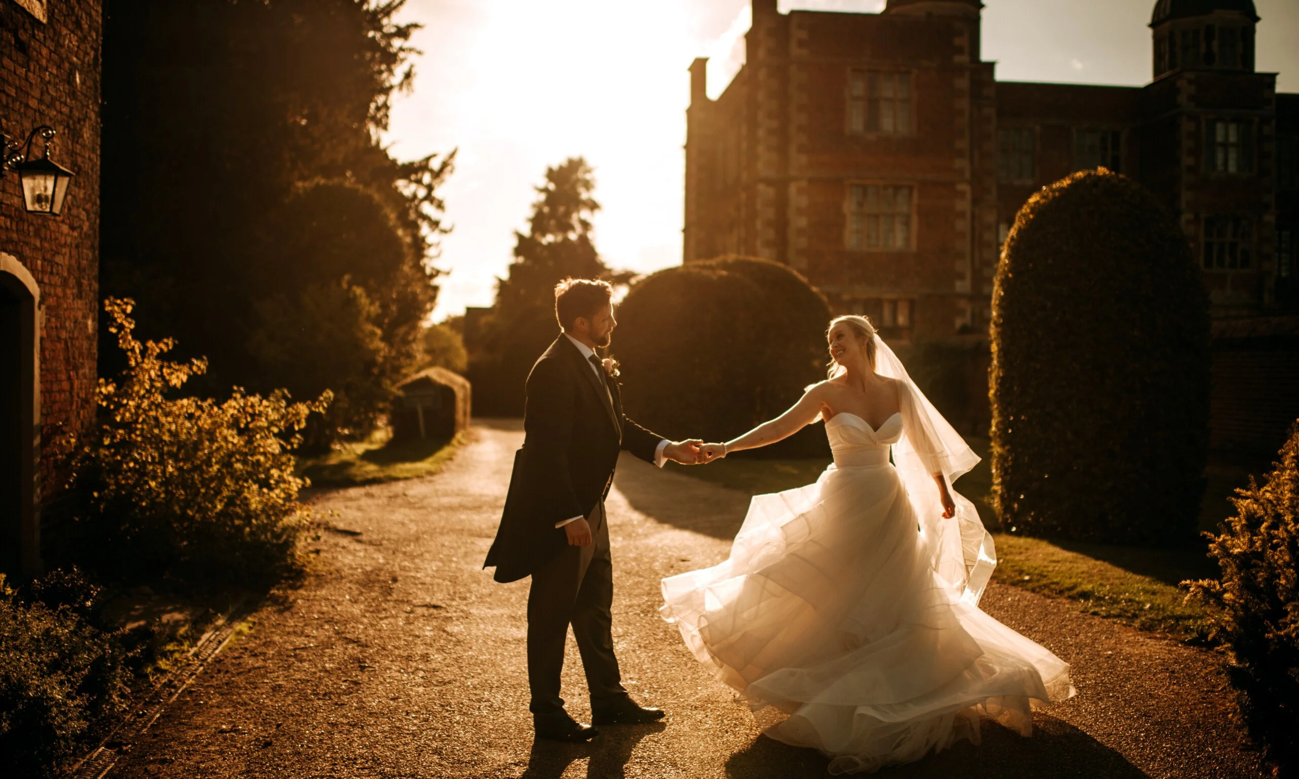 a bride and groom holding hands in the sunset with elizabethan hall in the background