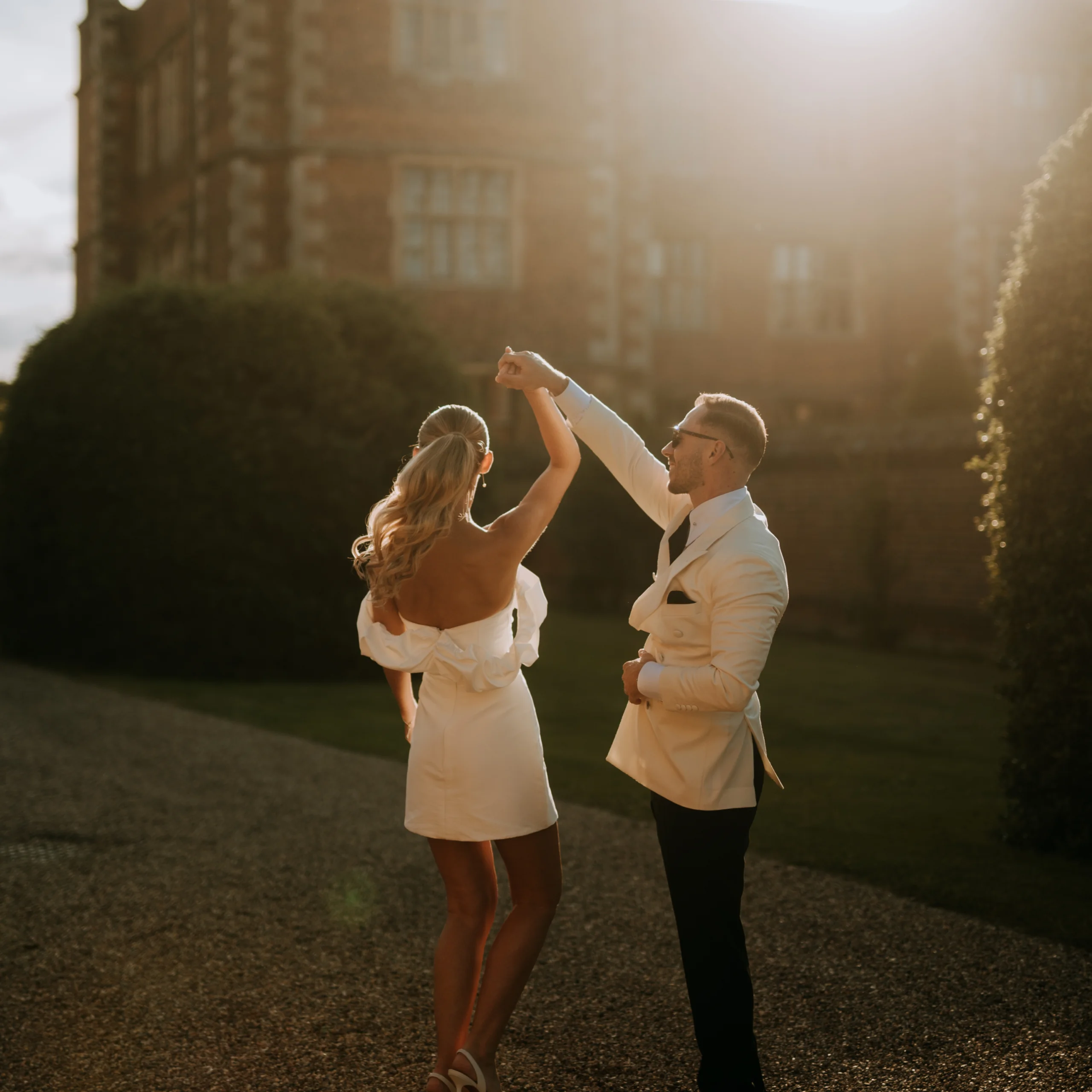 a bride and groom dancing in the sunset lighting in front of doddington hall
