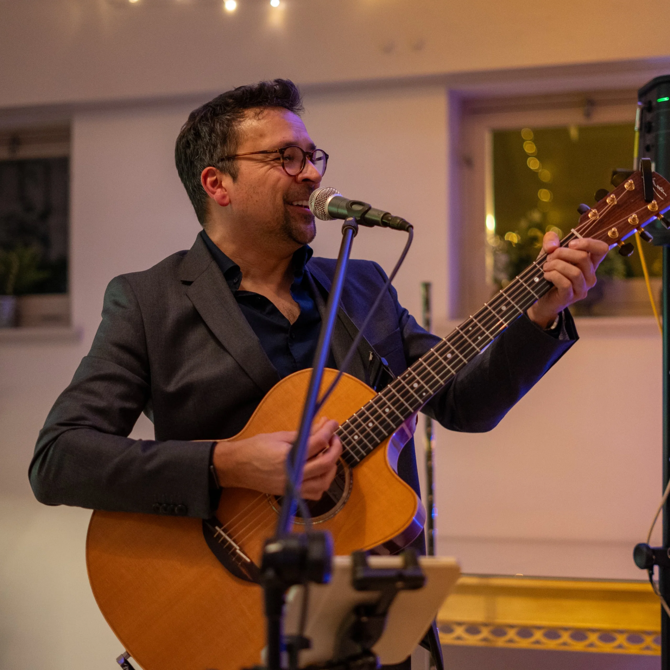 male wedding singer holding an acoustic guitar smiling and singing into a microphone