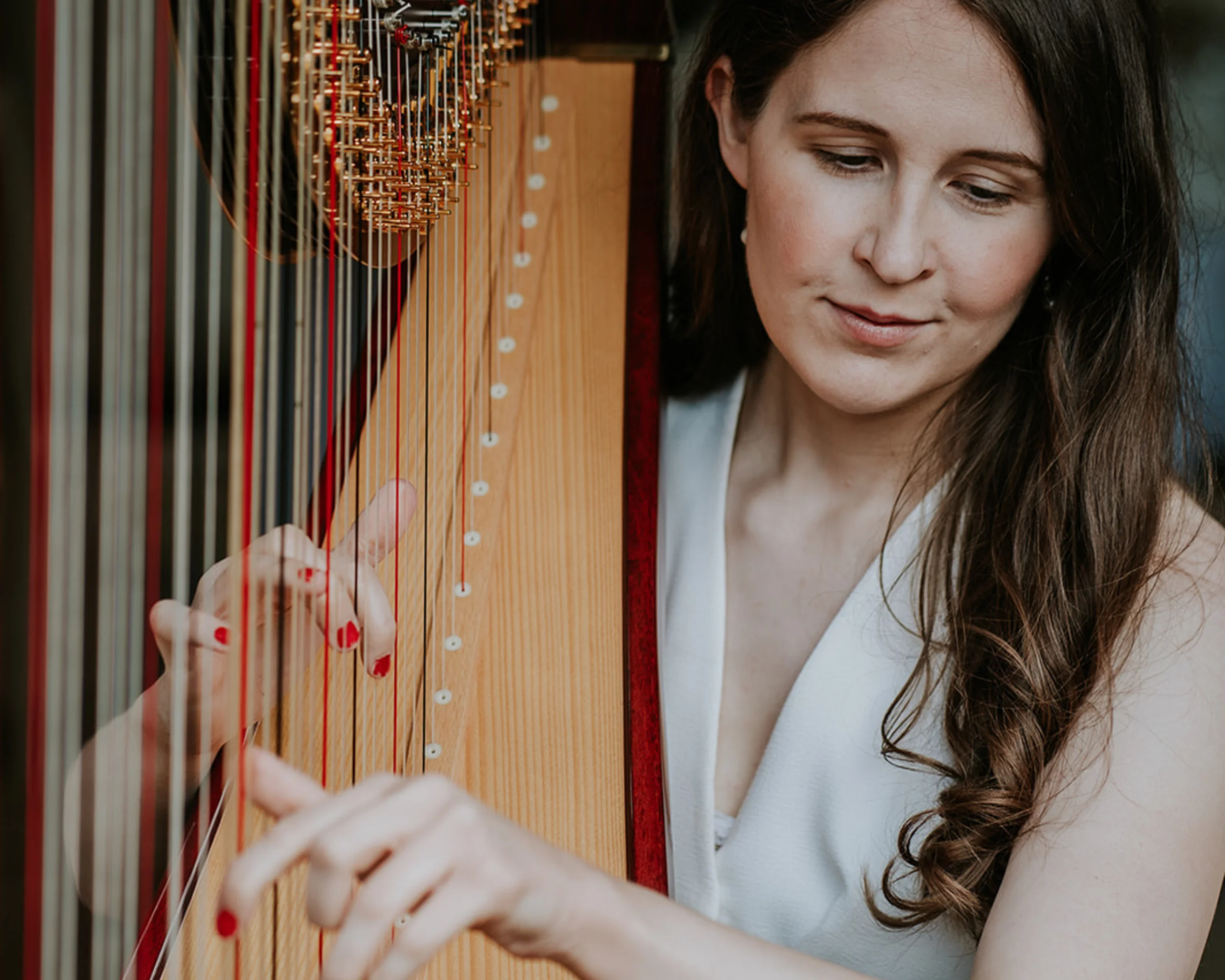 a lady wearing a white waistcoat strumming a harp with red nail varnish on her finger nails