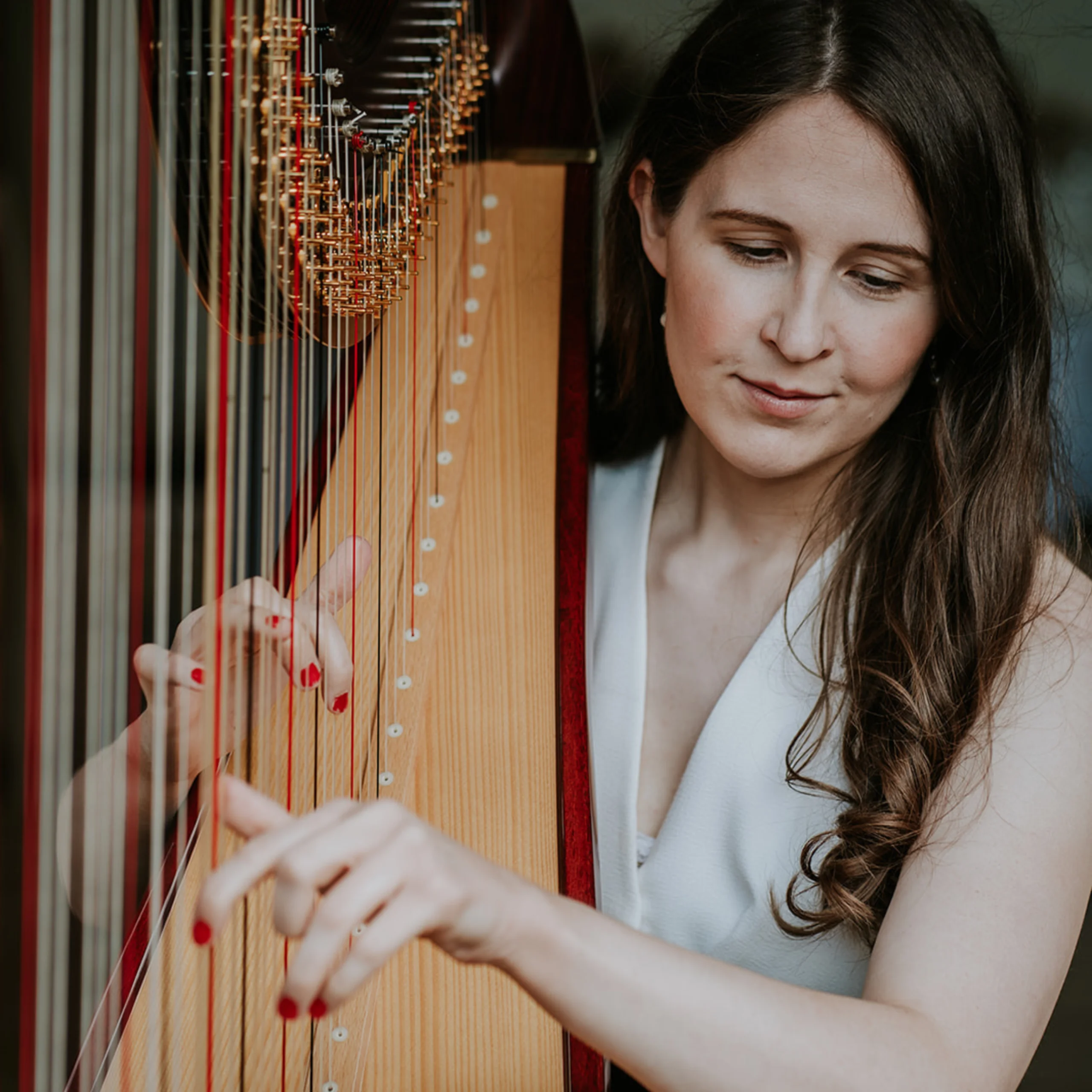 a lady wearing a white waistcoat strumming a harp with red nail varnish on her finger nails