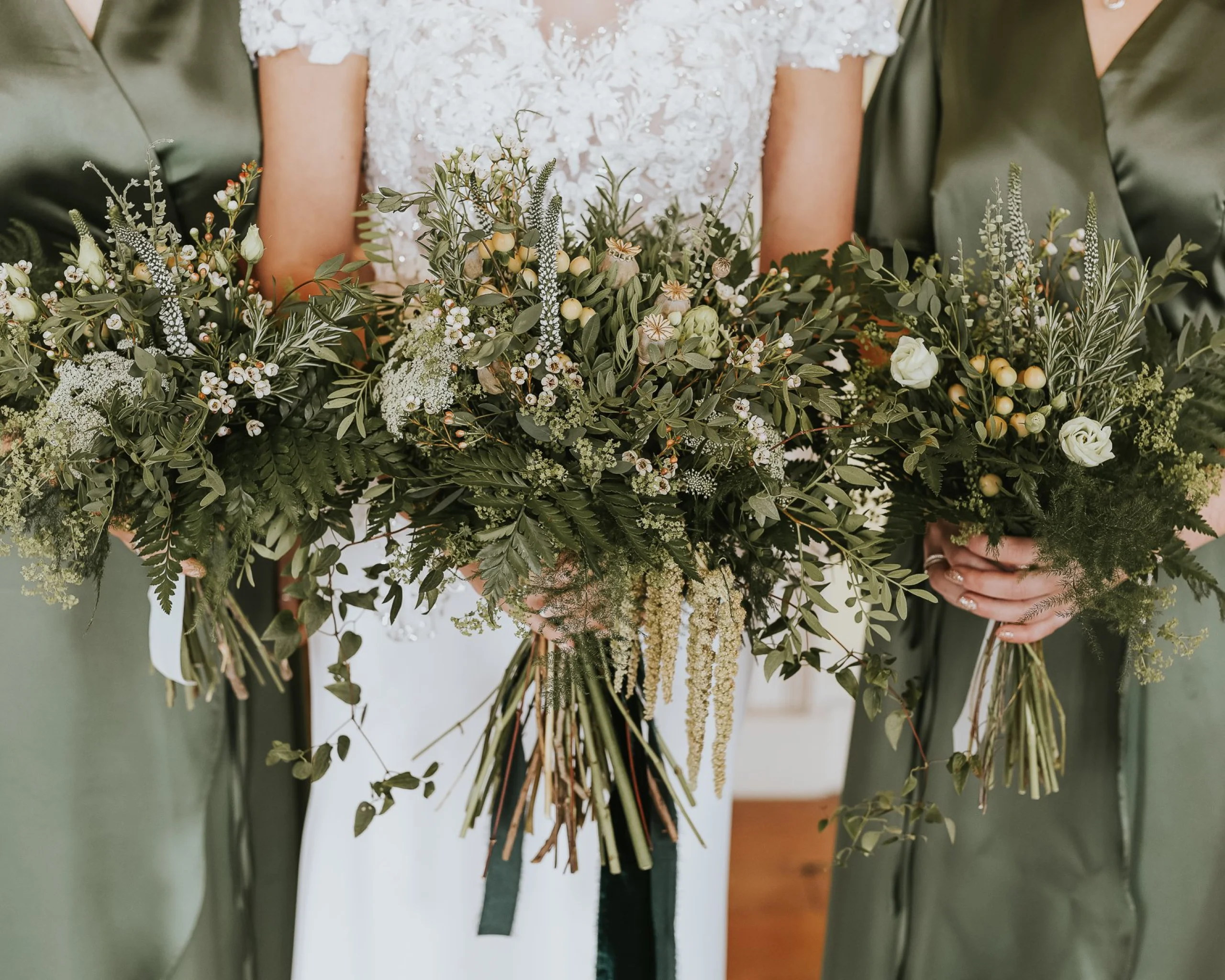 a bride and two bridesmaids holding bouquets with foliage and dainty white flowers