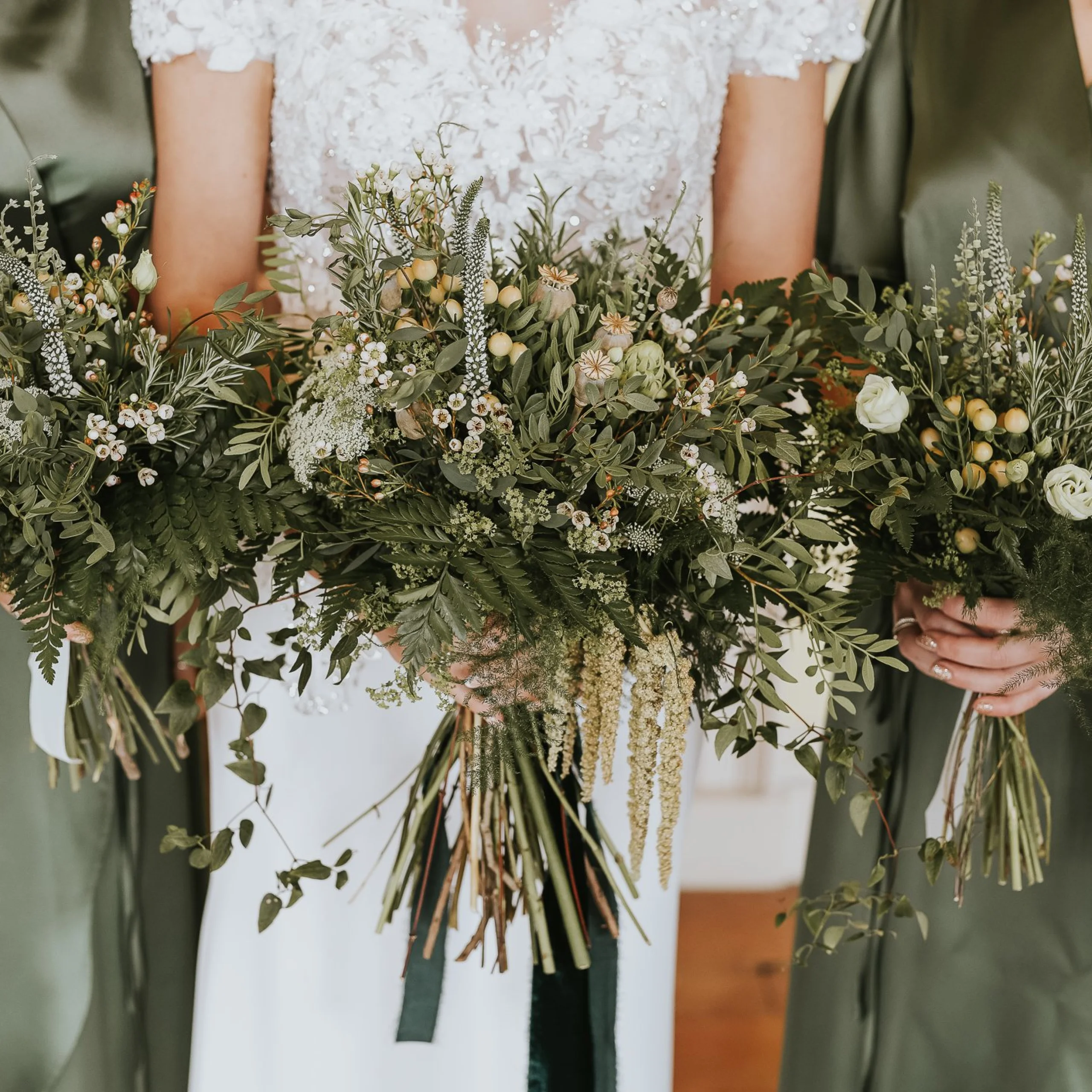 a bride and two bridesmaids holding bouquets with foliage and dainty white flowers