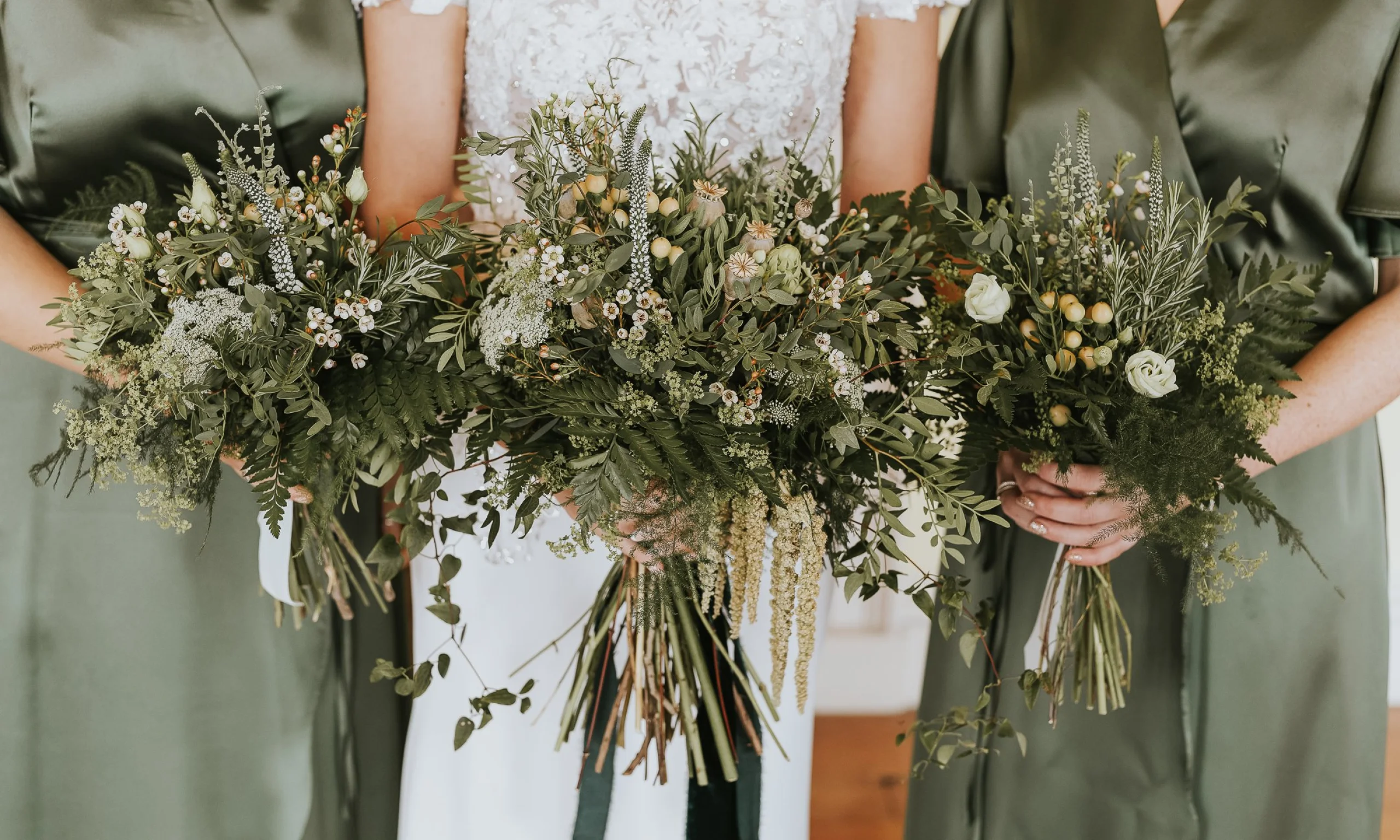 a bride and two bridesmaids holding bouquets with foliage and dainty white flowers