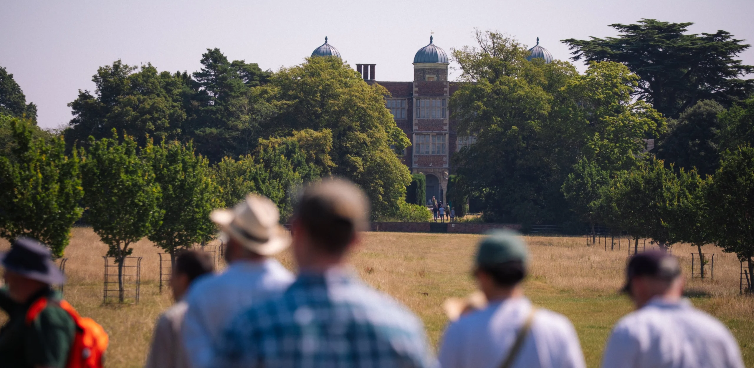 people walking through grass meadows on the doddington estate looking back at the elizabethan hall