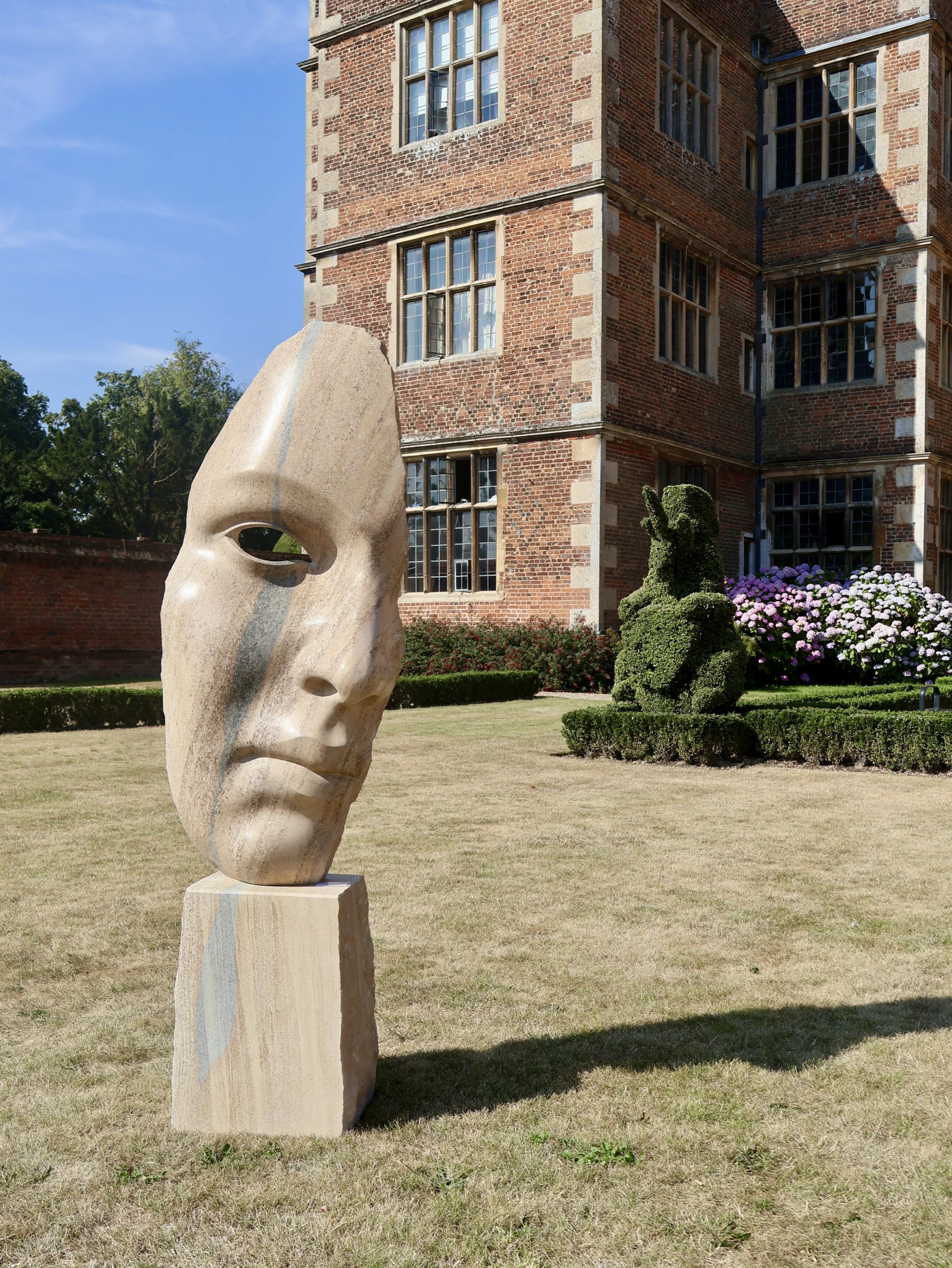 a sculpture of a womans face on the lawn in front of doddington hall