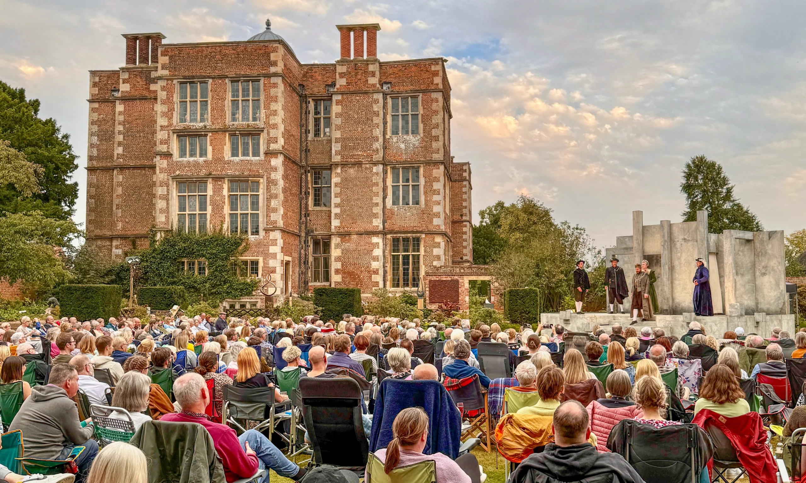 lots of people sat on camp chairs in the ground of doddington hall enjoying a theatre performance