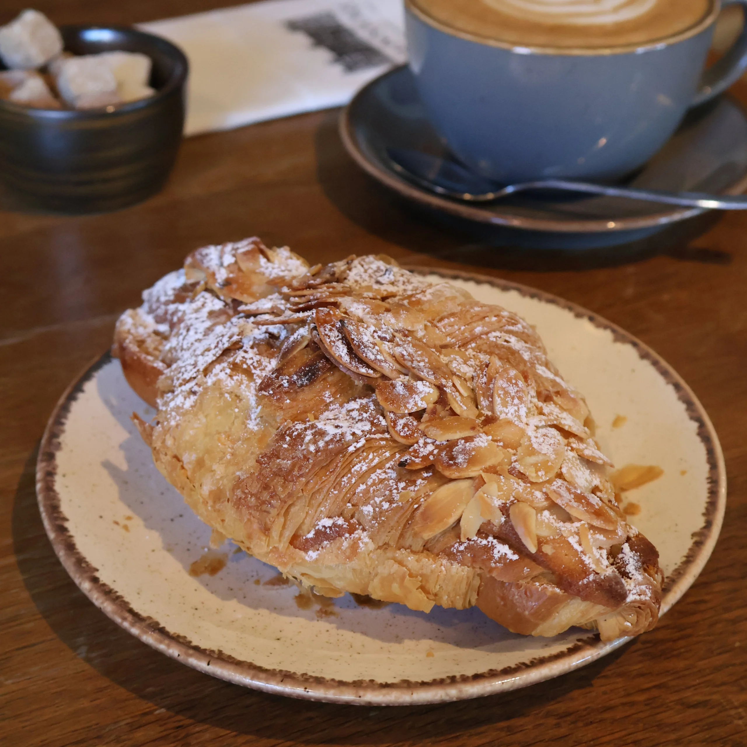 an almond criossant on a plate dusted with icing sugar
